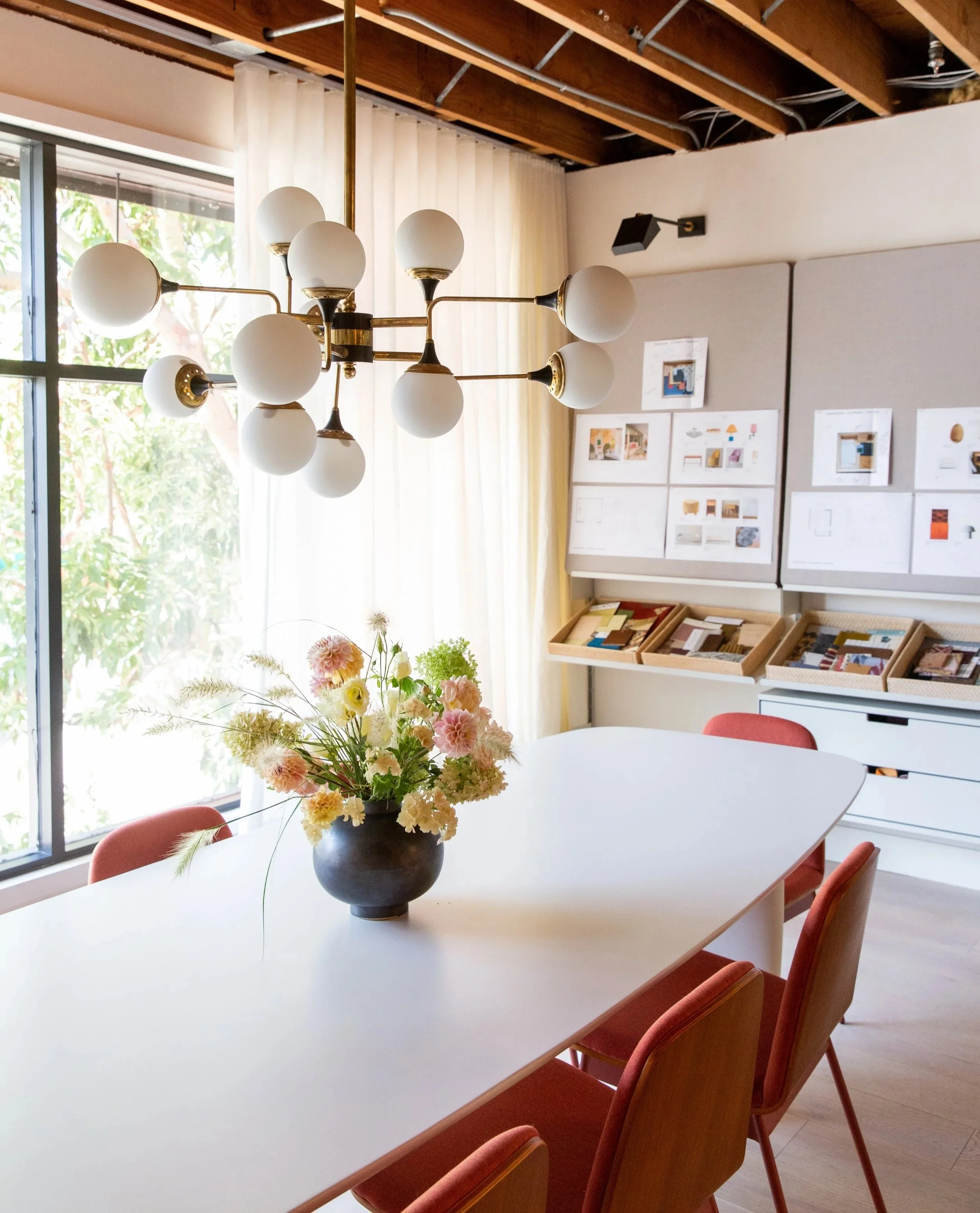Beautiful interior designers office with large windows, table with modern light fixture and flower arrangement and  mood board on wall
