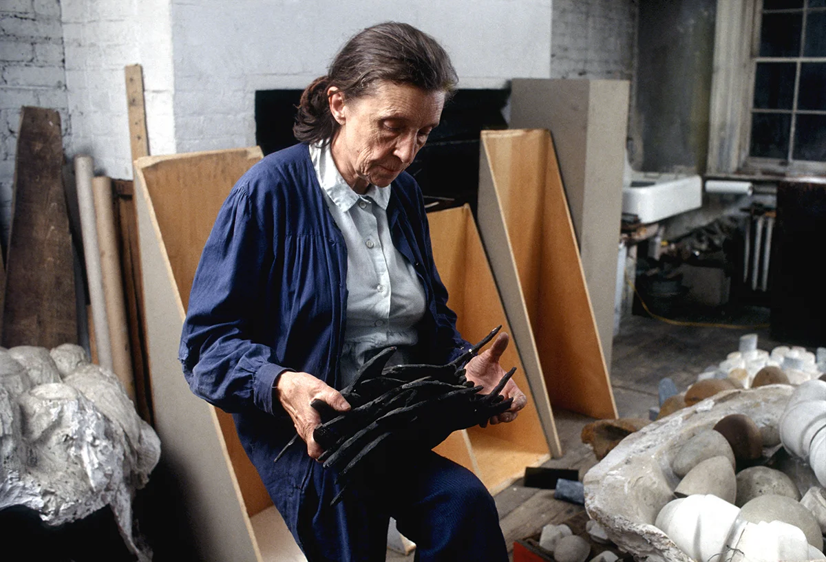 Bourgeois holding her sculpture, Blades (1969). In the background are elements for Confrontation (1978) and plaster works in progress in her home studio on 20th Street in New York, 1974. Photo: Mark Setteducati; © The Easton Foundation/Licensed by VAGA at ARS, NY
