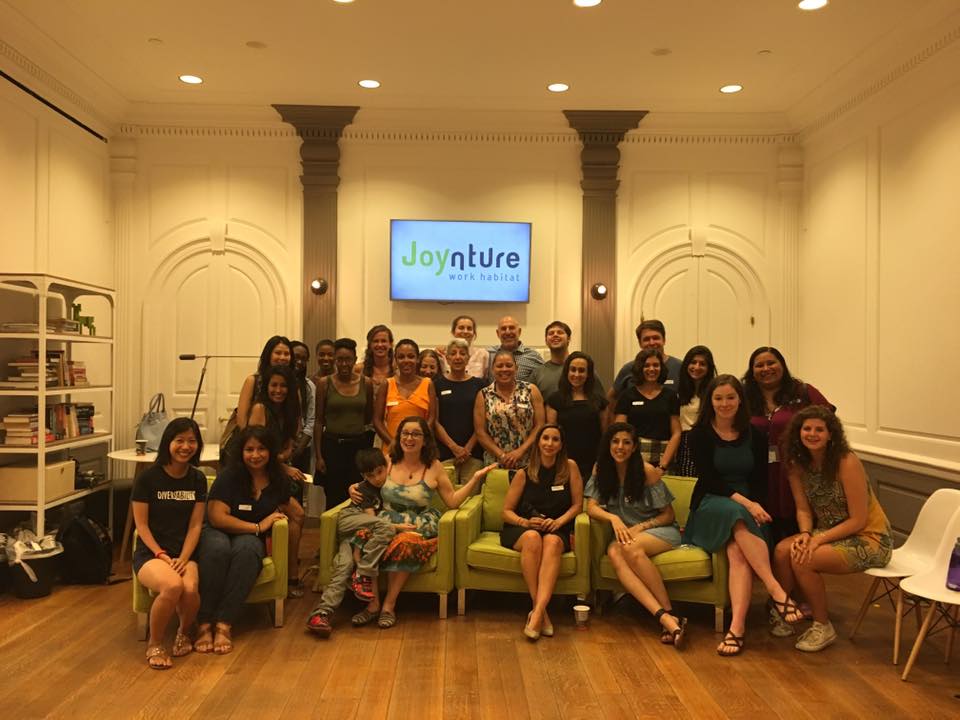 Photo of event attendees and speakers, with speakers sitting in the front in lime green chairs and two rows behind them.