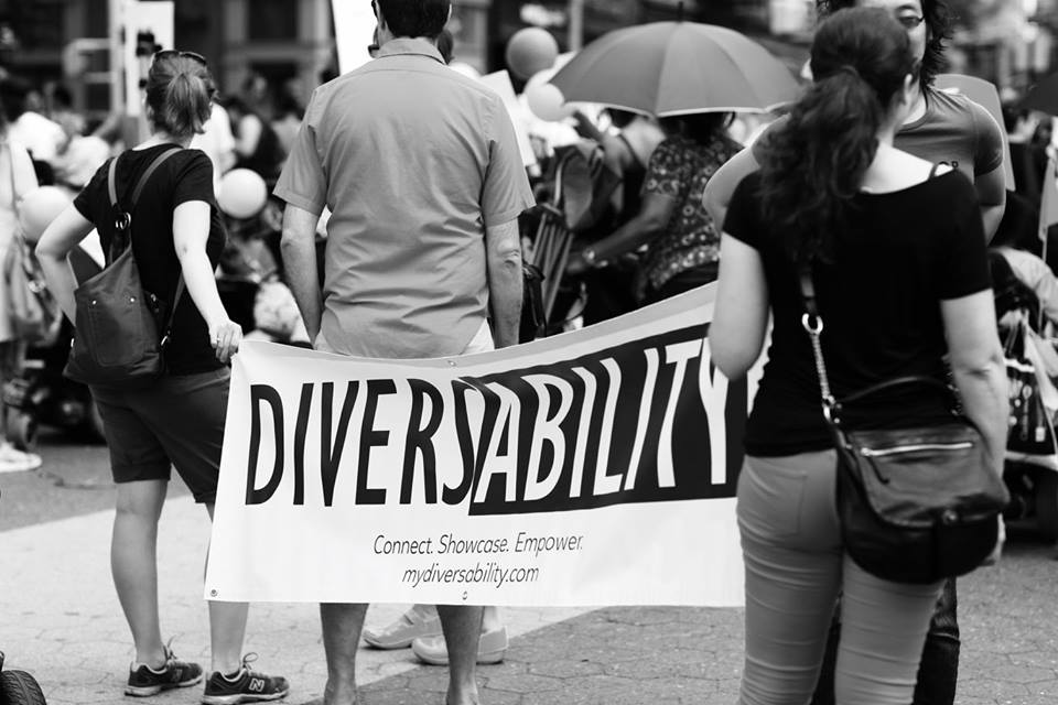 Black and white image of Diversability flag carried by two individuals. 