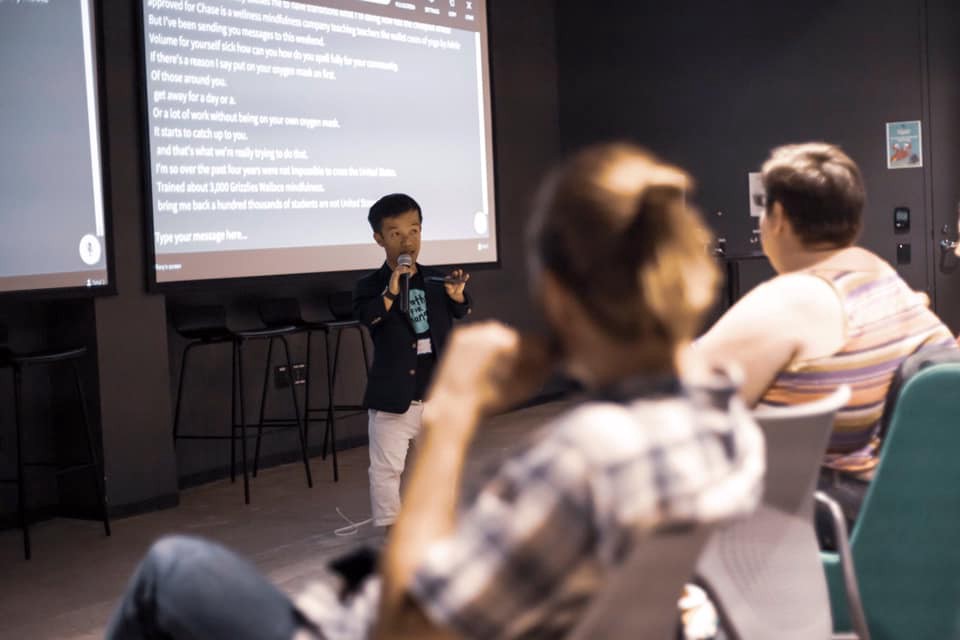 Danh Trang speaking into a microphone with captions in white on the screen behind him. Photo credit: Kai Faust