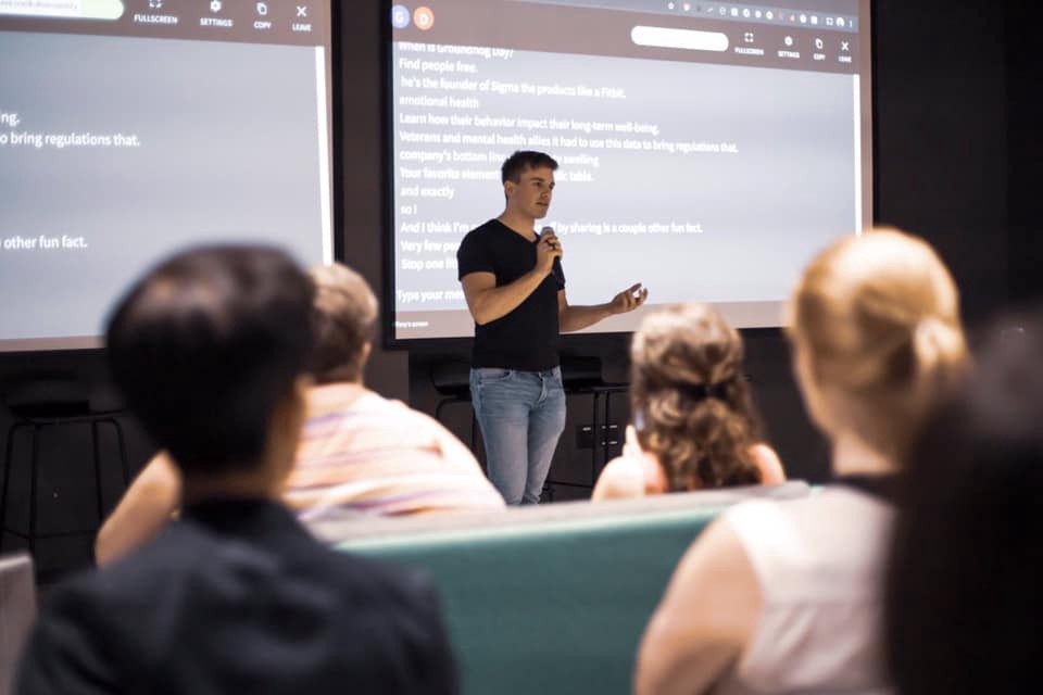 Dan Seider speaking into a microphone with the screen of captions behind him. Photo credit: Kai Faust