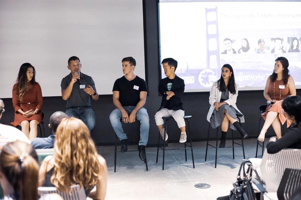 Panel of 6 people seated in tall chairs at the front of the room. Photo credit: Kai Faust