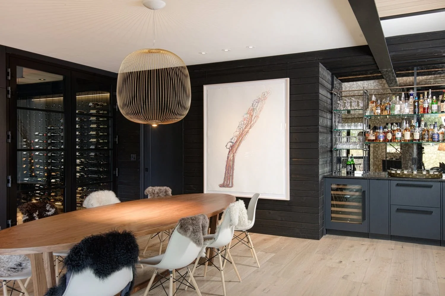 Walk-in wine cellar with stone wall and cable racking beside a custom home bar by Sommi