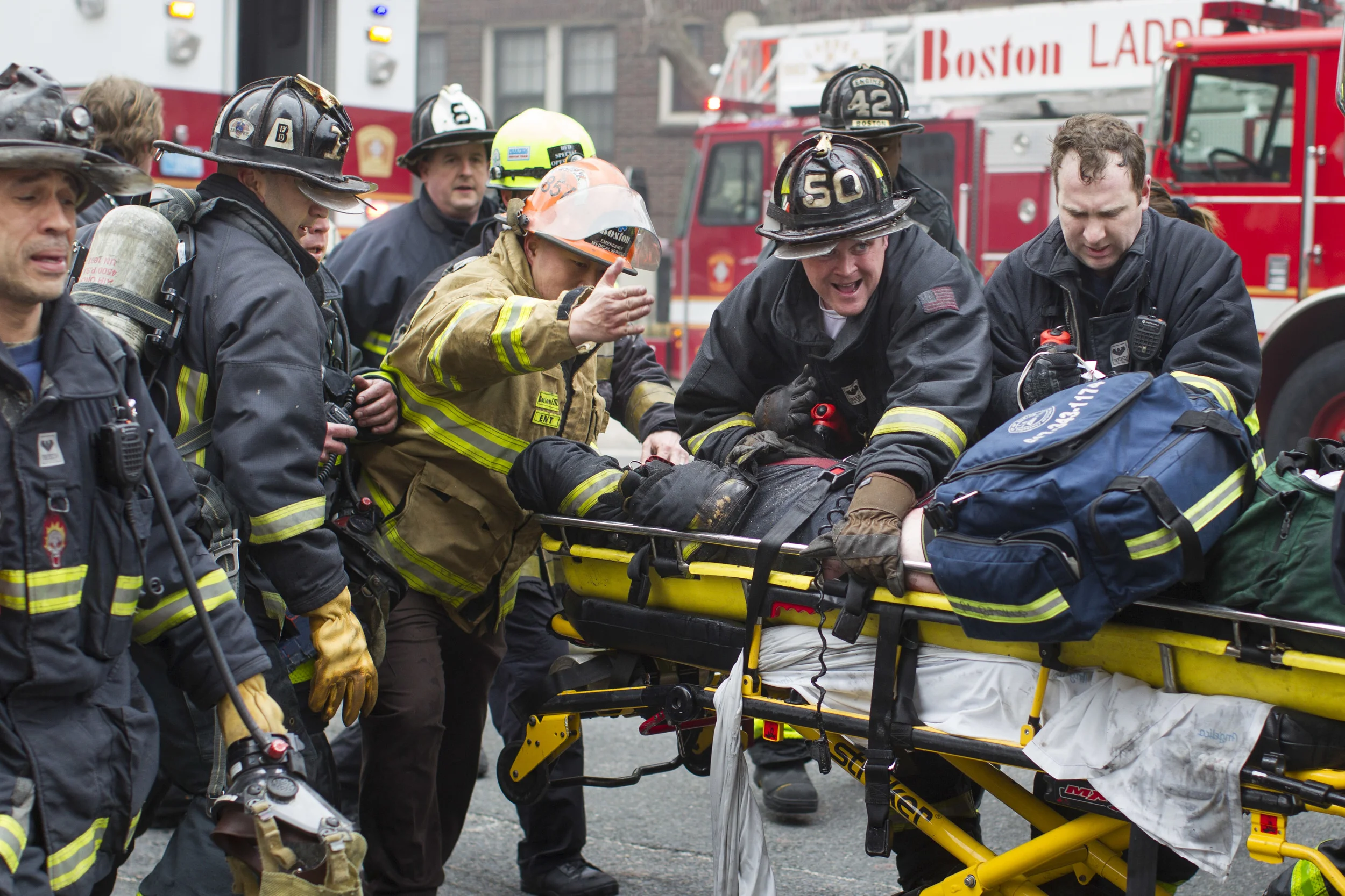   Firefighters and emergency medical personnel rush a firefighter from the scene of a multi-alarm fire at a four-story brownstone in the Back Bay neighborhood near the Charles River, Wednesday, March 26, 2014, in Boston. The fire left two firefighter