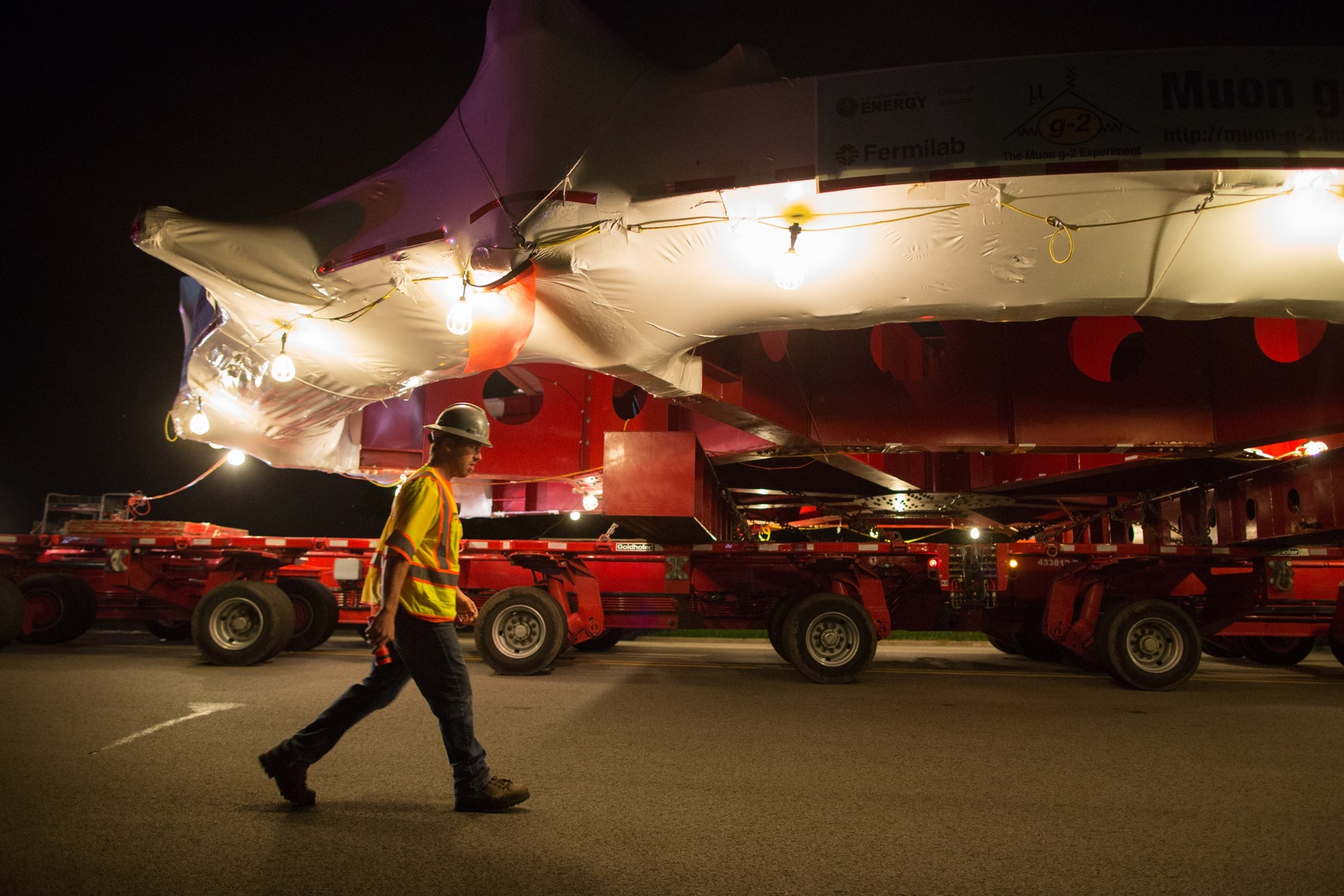 A worker walks underneath the electromagnet as it moves down Butterfield Road in Glen Ellyn, Ill., Thursday, July 25, 2013 enroute to its new home outside Chicago on Friday. The electromagnet is 50 feet wide, weighs more than 15 tons and has taken a month to transport 3,200 miles from New York to Illinois.