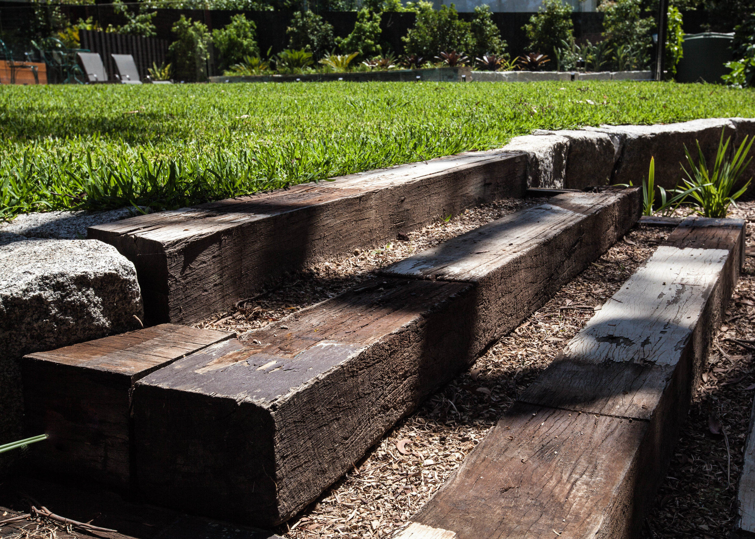 Recycled timber steps lead up from the sunken campfire lounge to the lawn area. Bolstered granite blocks serve as retaining walls to give the lawn a lift and to tie in with the granite in the pool area.
