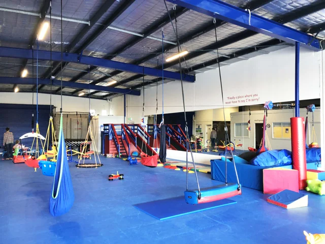 Indoor sensory gym in Preston showing suspended swings, blue padded flooring and play equipment