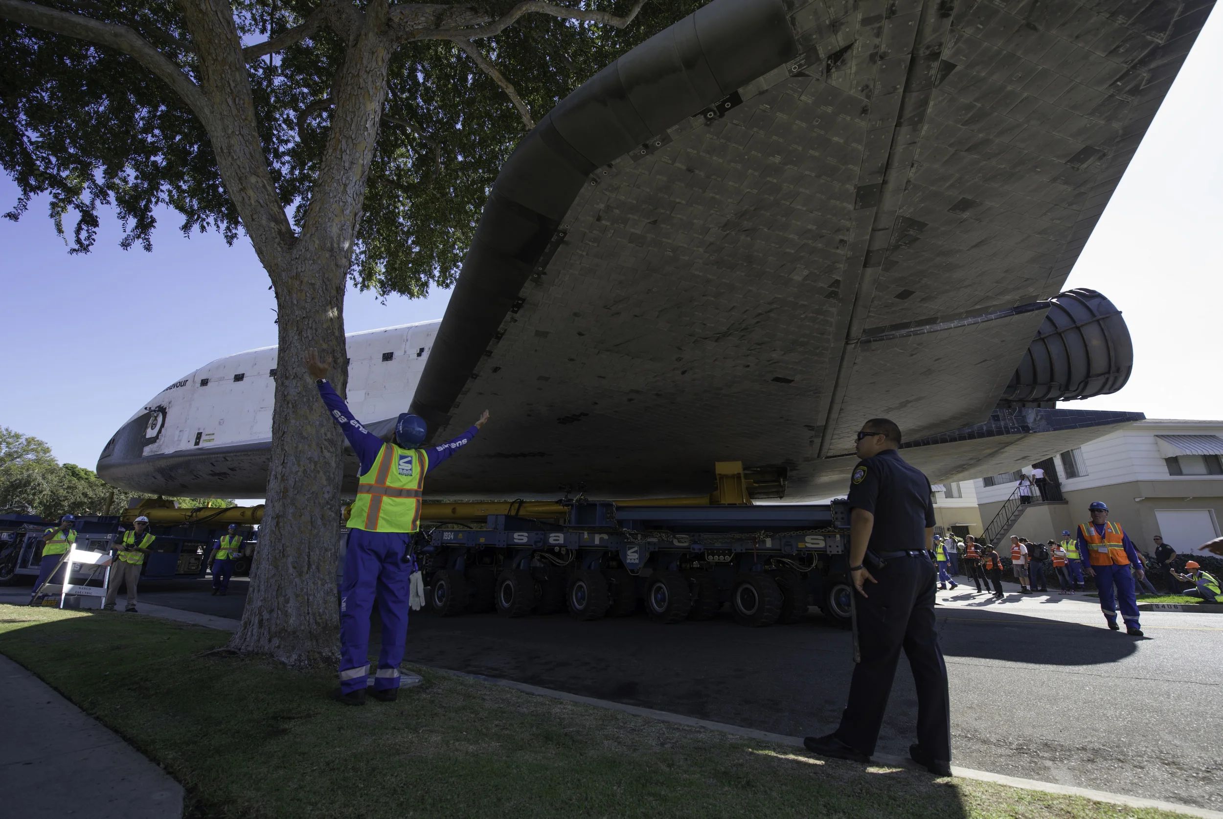 A technician for the Over Land Transporter (OLT) carrying the space shuttle Endeavour signals how much room is available between a tree and the orbiter’s wing, Saturday, Oct. 13, 2012, as it maneuvers its way through the streets of Inglewood, Calif. Endeavour, built as a replacement for space shuttle Challenger, completed 25 missions, spent 299 days in orbit, and orbited Earth 4,671 times while traveling 122,883,151 miles. Beginning Oct. 30, the shuttle will be on display in the CSC’s Samuel Oschin Space Shuttle Endeavour Display Pavilion, embarking on its new mission to commemorate past achievements in space and educate and inspire future generations of explorers. (NASA/Carla Cioffi)