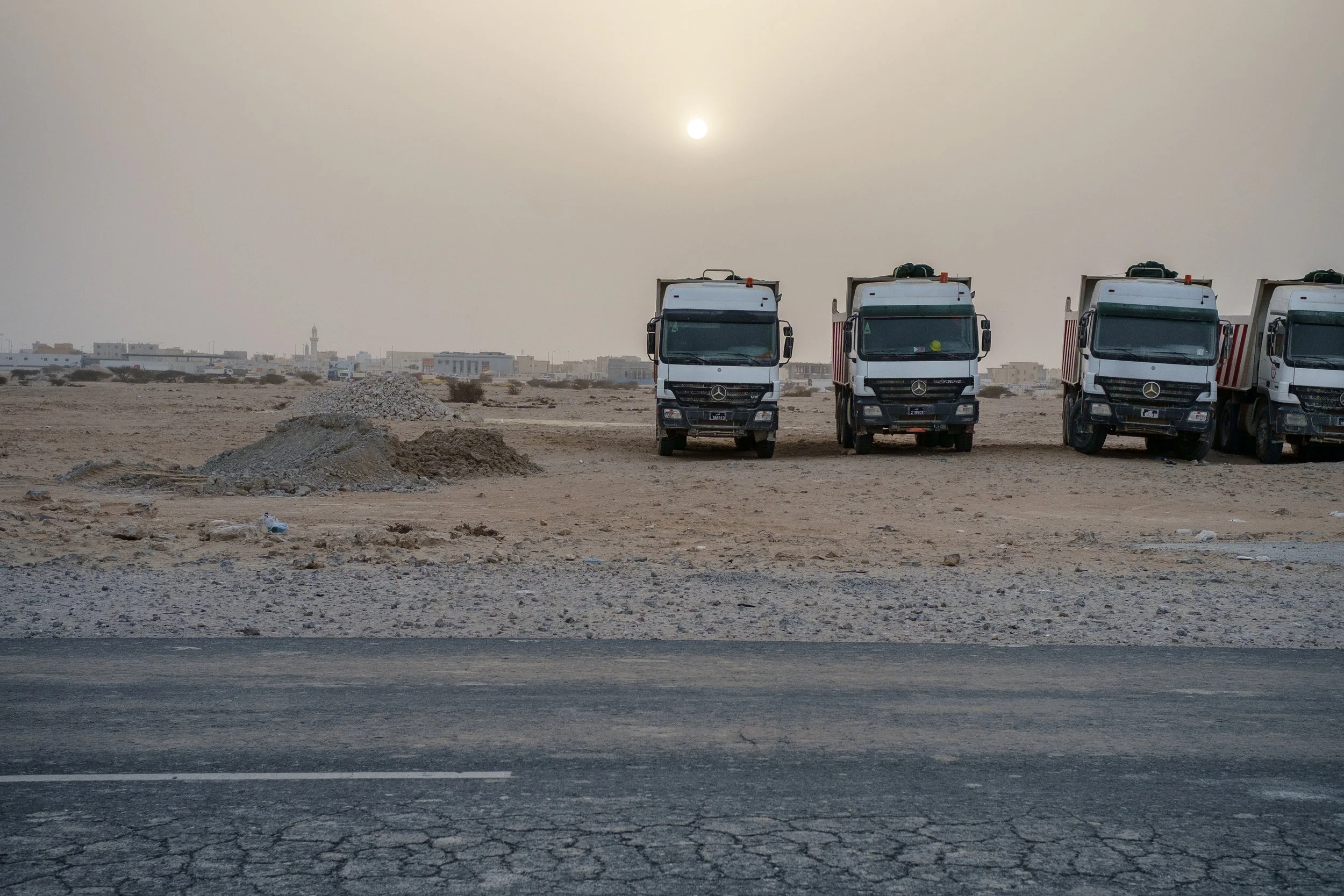 Dumpster trucks are lined up on their day off as the sun sets behind them. Desert dust is often in the air creating an other-worldly atmosphere.