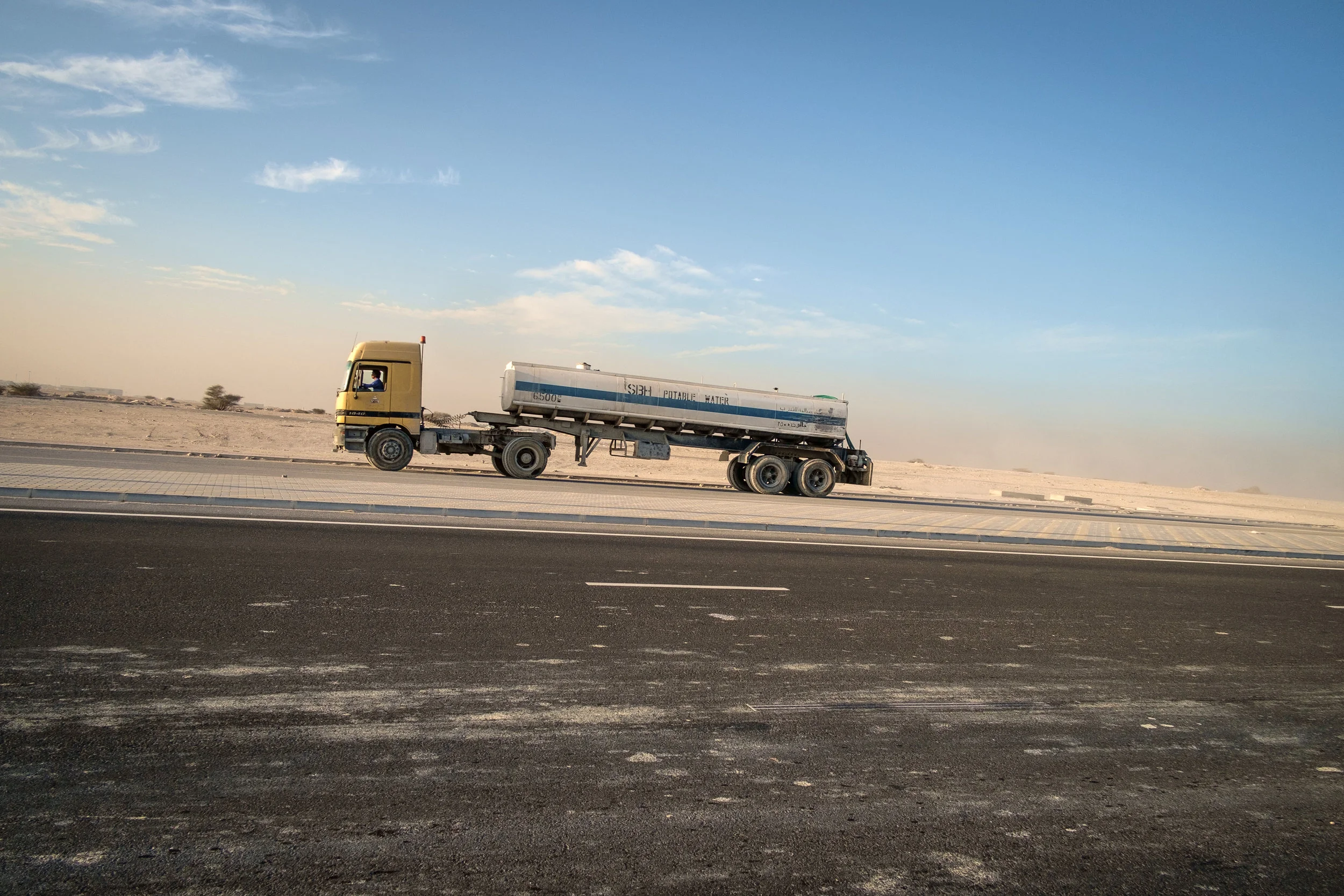 The ubiquitous semi truck, this one carrying water, is seen at sunset leaving massive construction site on the outskirts of Doha.