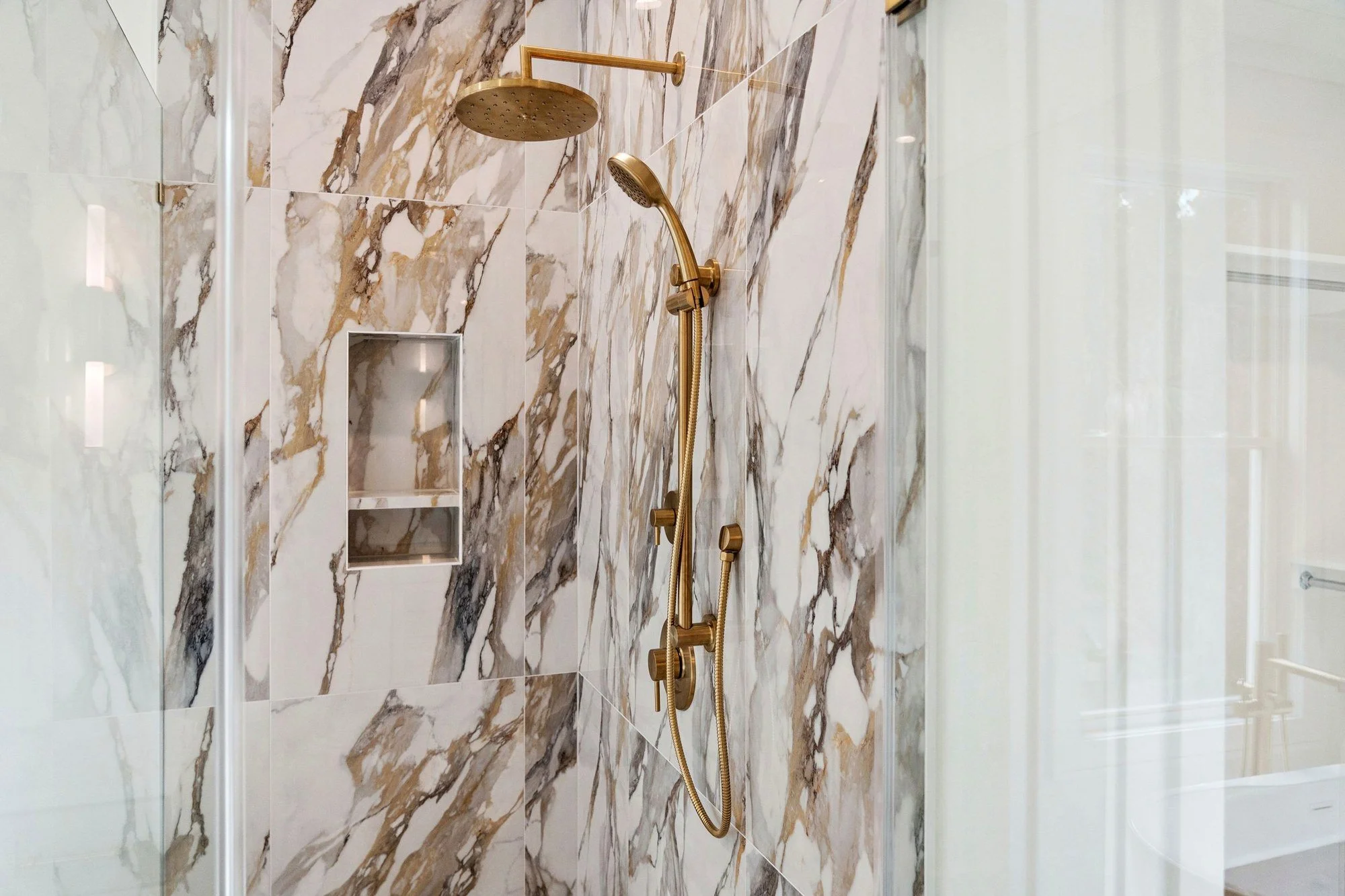 Primary shower with marble tile and brass fixtures in an Isle of Palms SC custom home