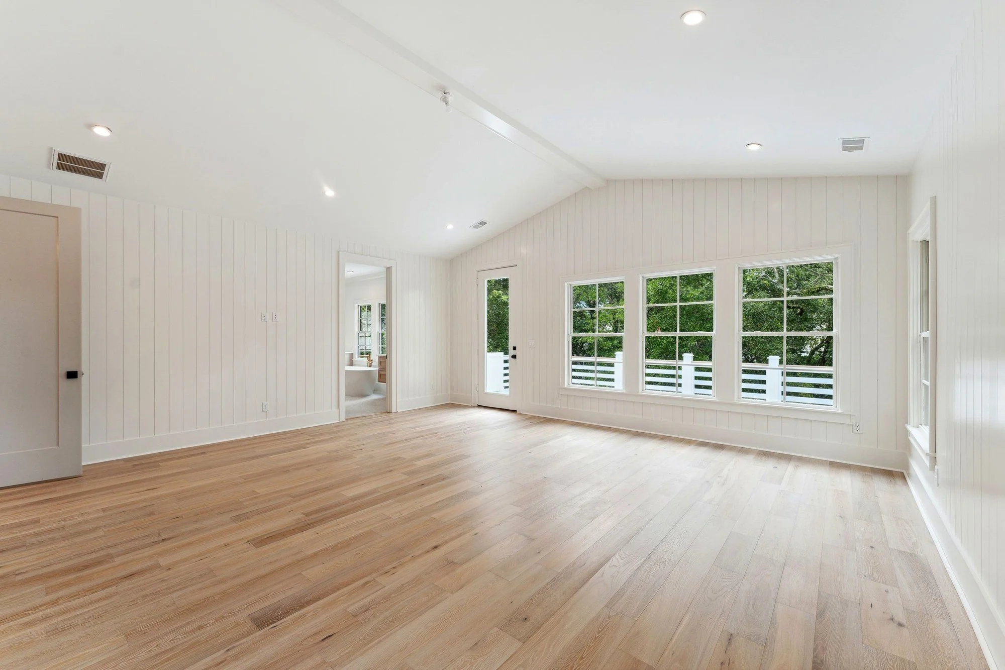 Bedroom with a vaulted ceiling and corner windows into the trees.