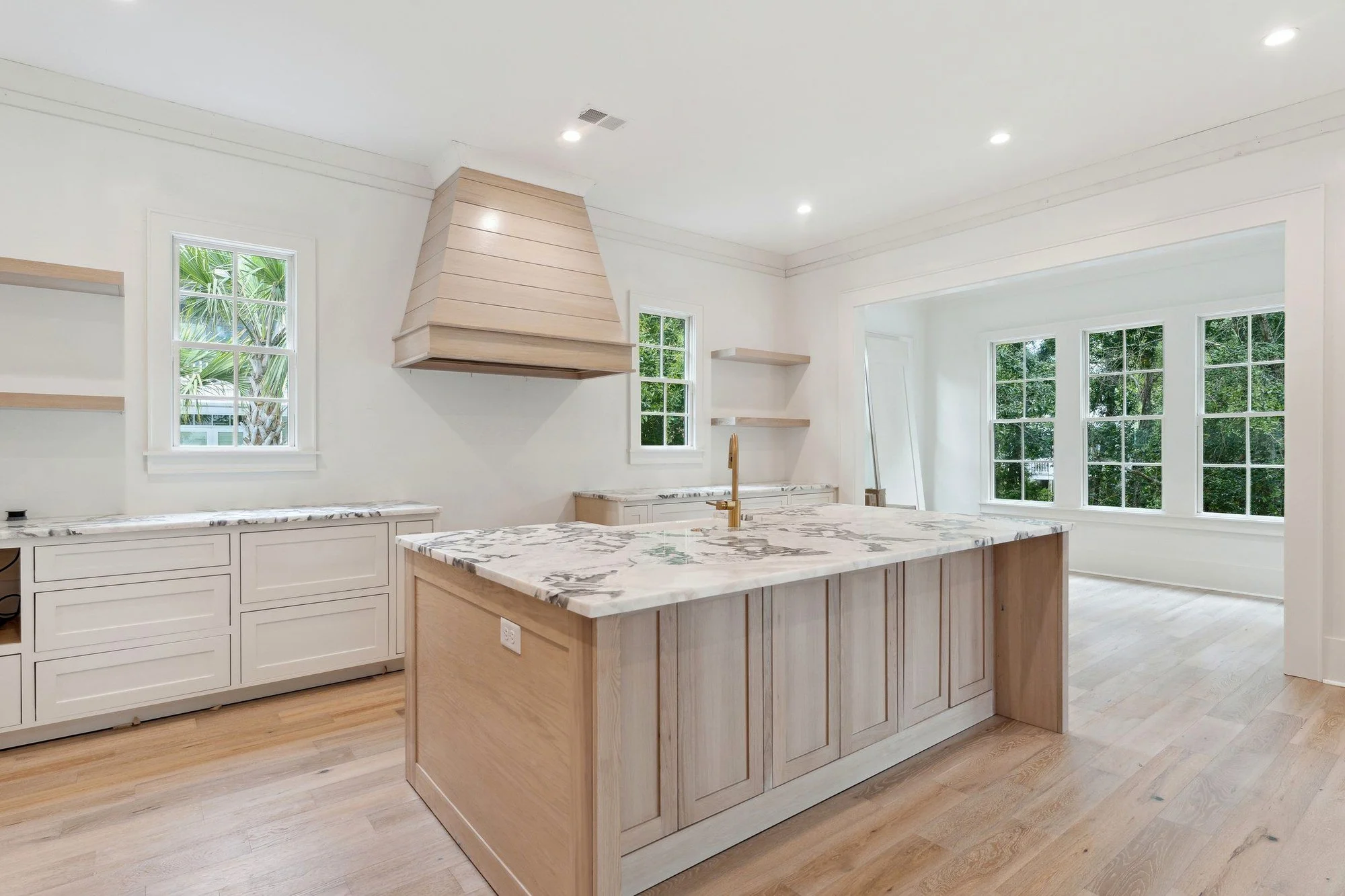 Kitchen with a whitewashed white oak island, book-matched marble counters and a shiplap range hood.