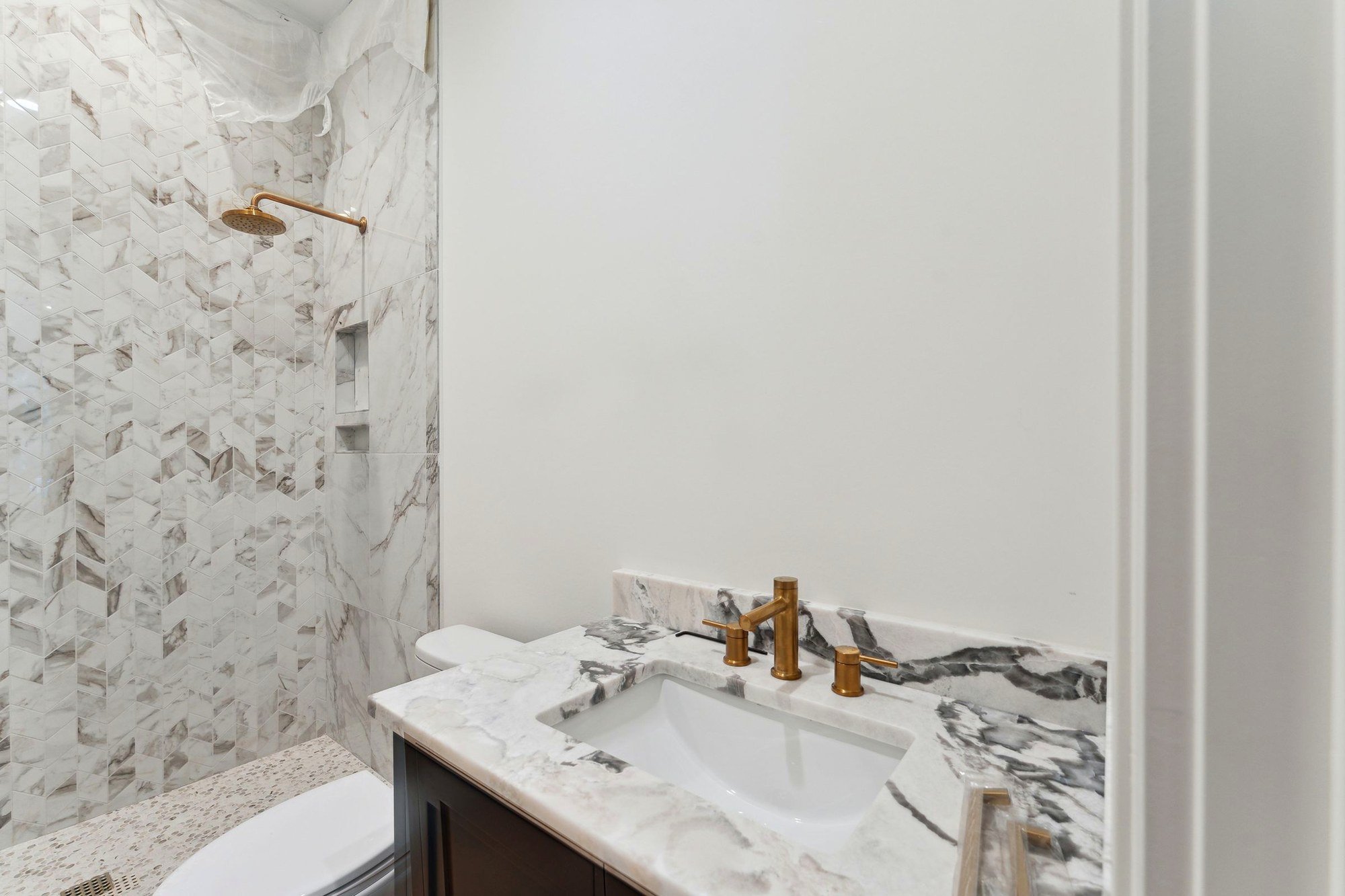 Guest bath with a marble mosaic shower, brass fittings and a marble vanity.