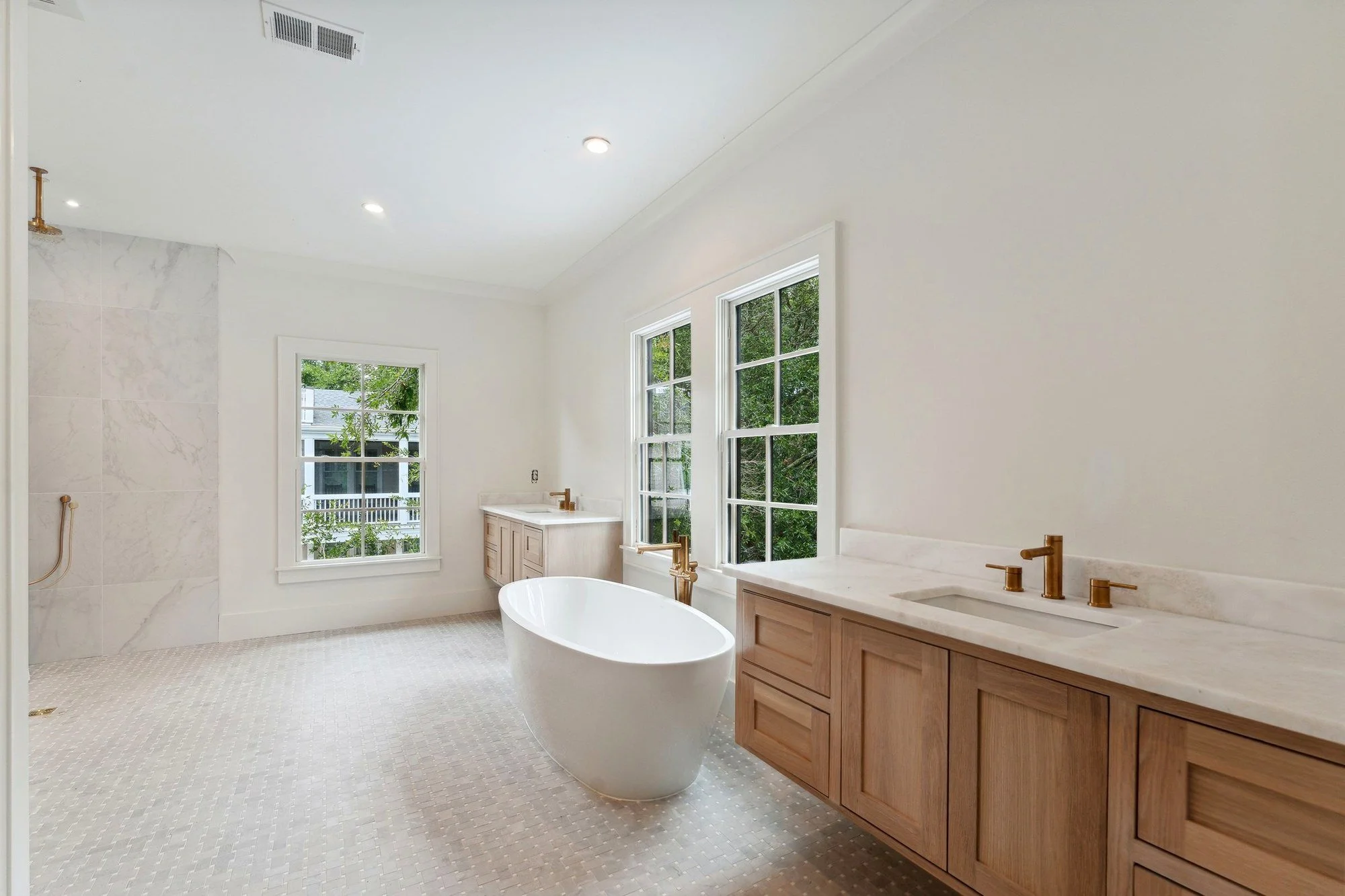 Owner's bath with a freestanding soaking tub between two white oak vanities.