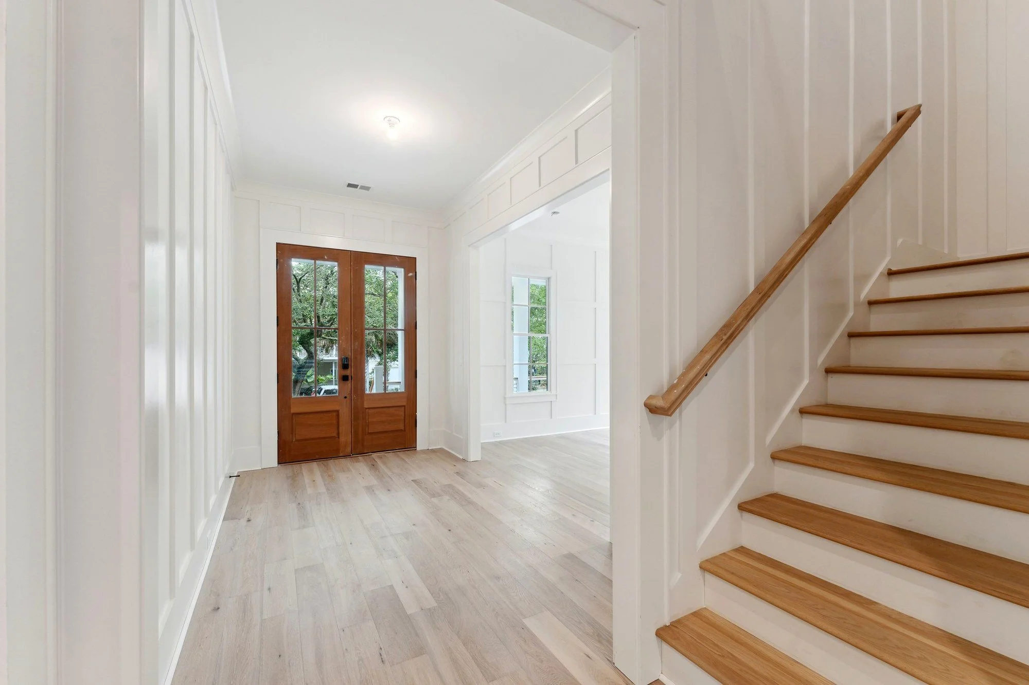 Entry hall in white oak with an open stair and full-height paneling.