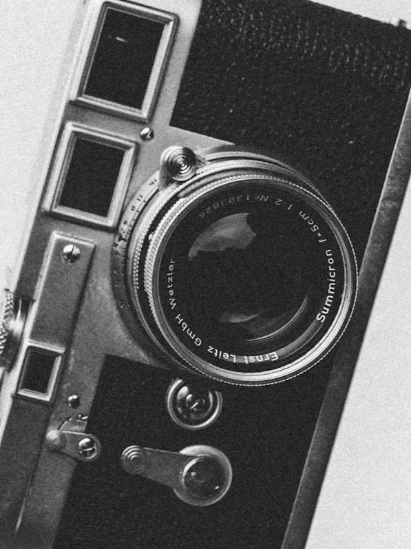 Close-up of a vintage camera with a prominent lens and film viewfinder in black and white.