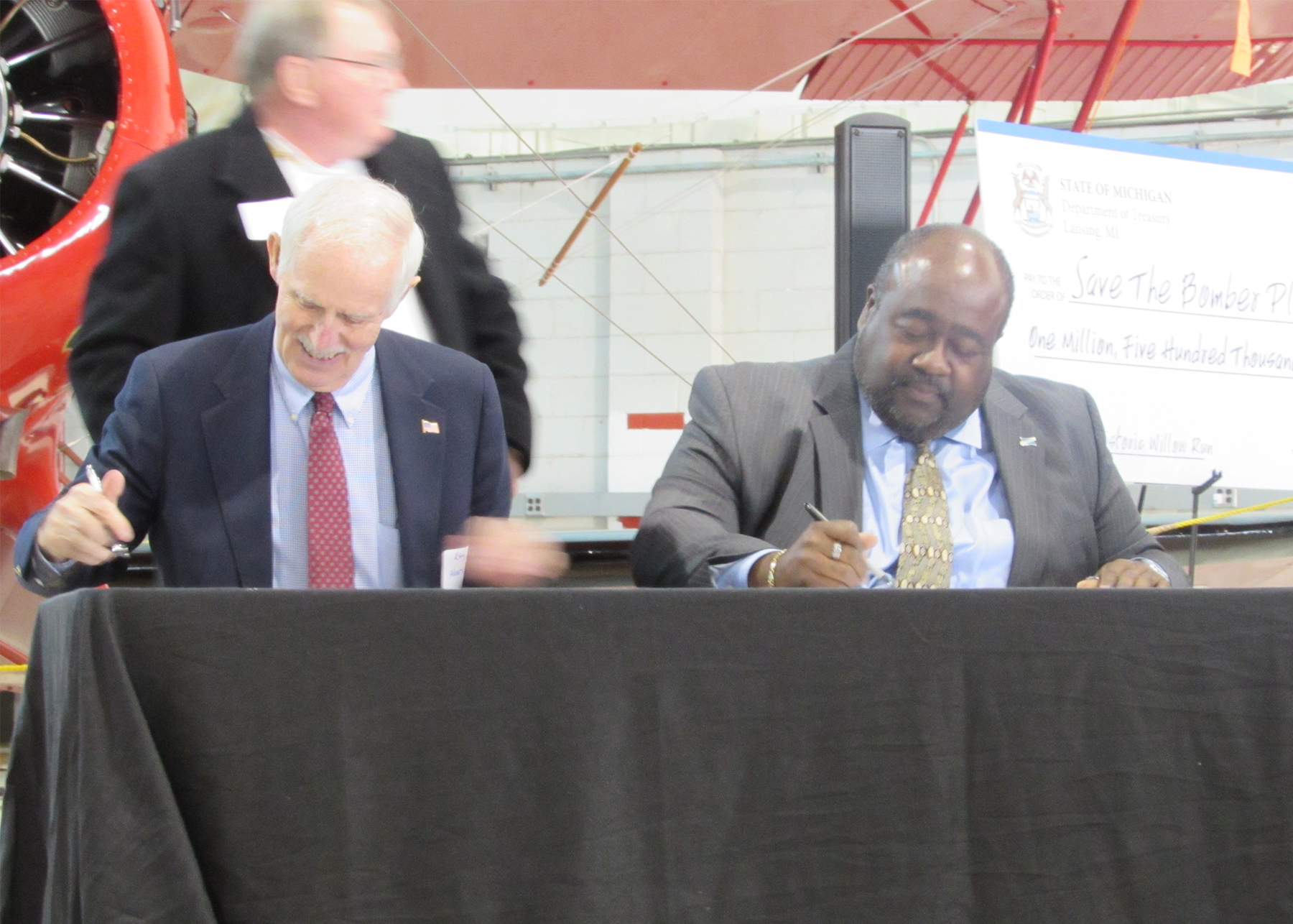 Ray Hunter of the Yankee Air Museum and Elliott Laws of RACER Trust sign documents transferring ownership of 144,000 sq. ft. of the former WIllow Run Bomber Plant to the Yankee Air Museum.