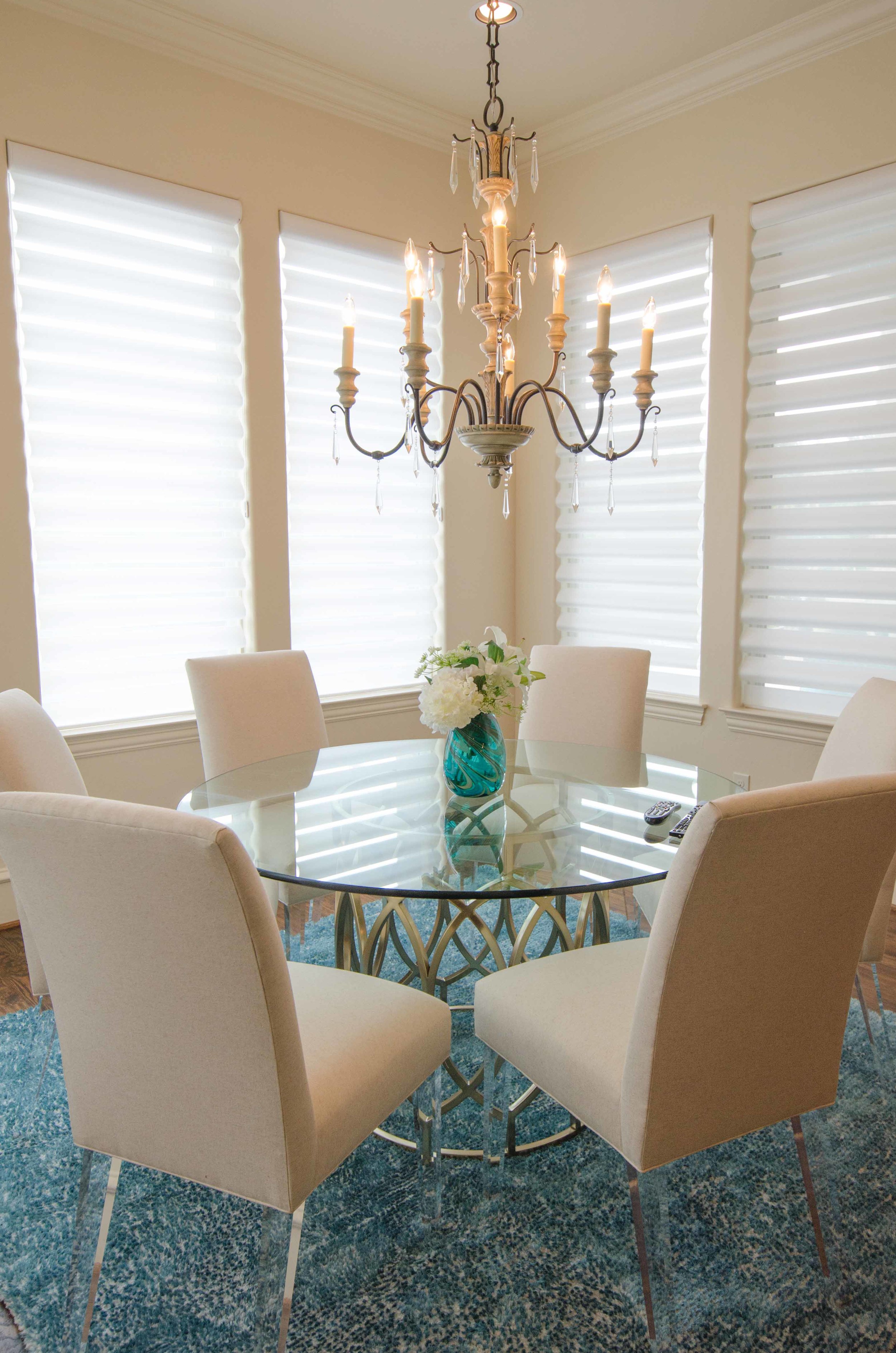 Transitional dining room with gold base and glass top table and chairs with lucite legs. Turquoise shag rug.