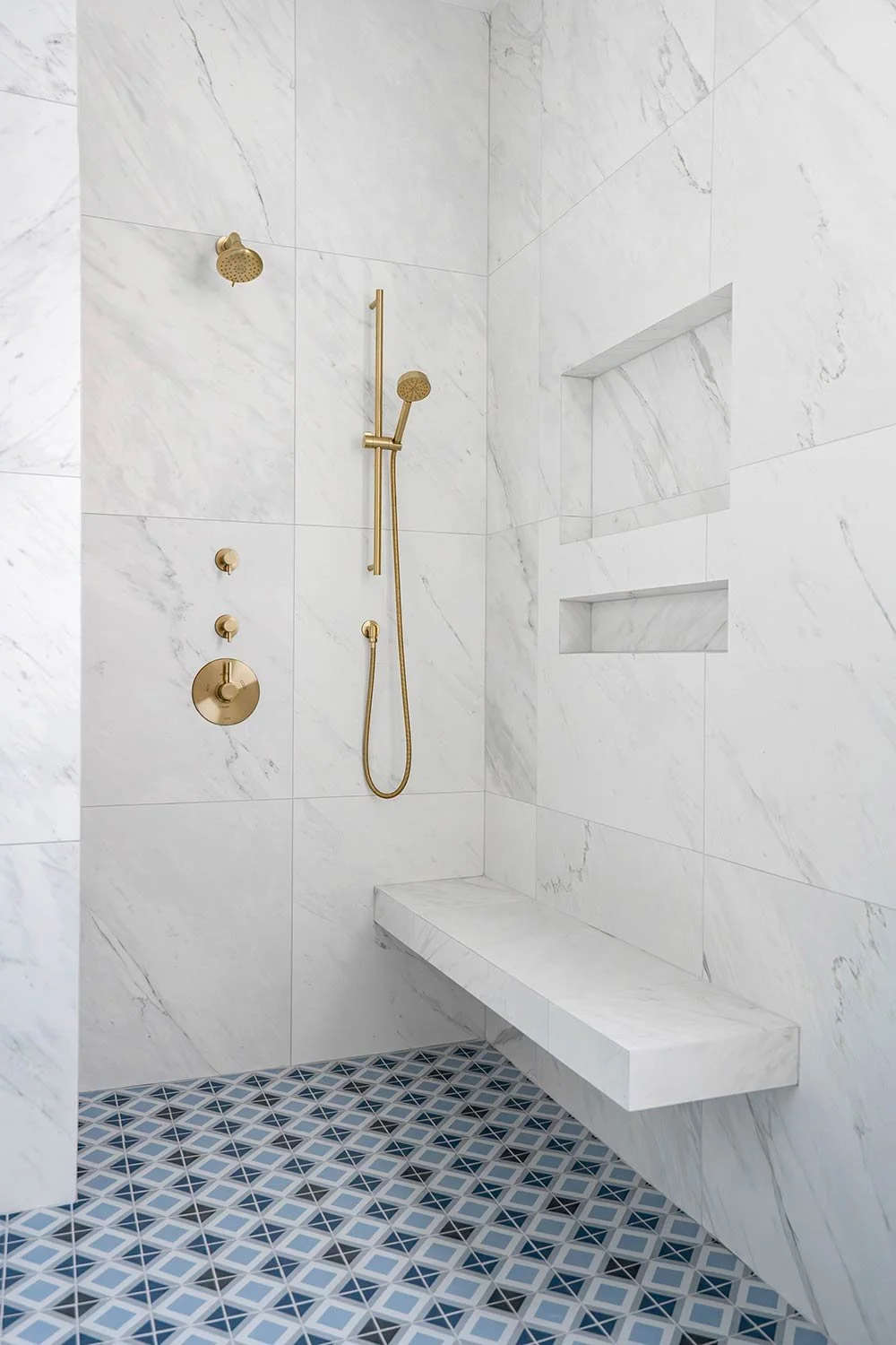 walk in shower with marbled wall and niches