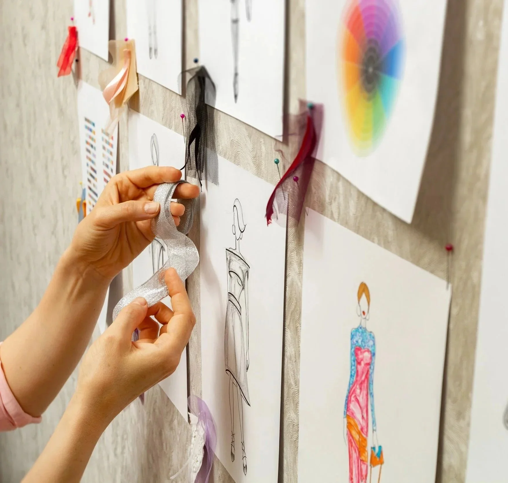Hands pinning fabric swatches to fashion design sketches