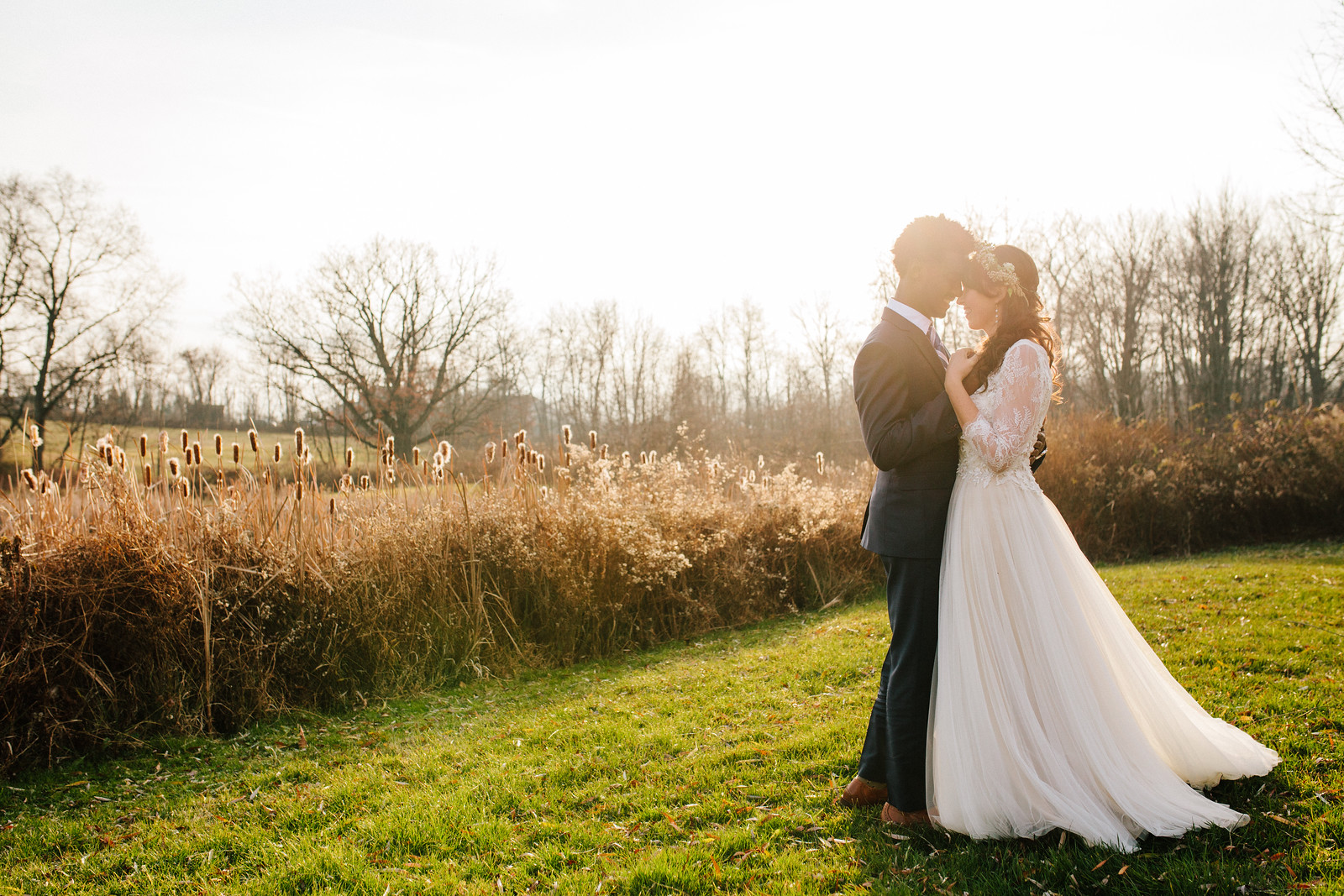 A Bride and groom standing in a meadow looking lovingly into each others eyes
