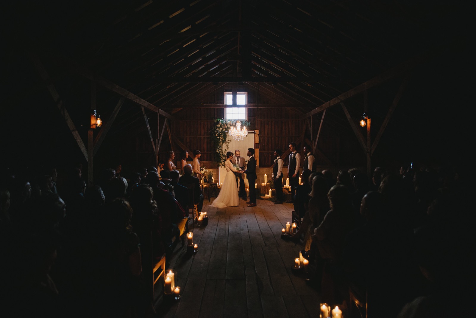 Romantic candlelit wedding ceremony in a barn with the bride and groom and wedding party