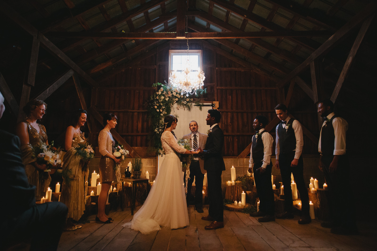 Winter barn wedding with candles, a floral arch, chandelier and the wedding party laughing