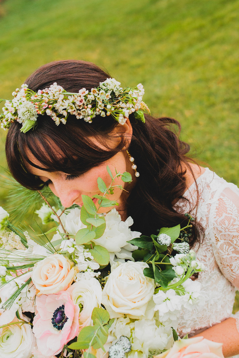 A bride wearing a simple floral crown with wax flower, lisianthus buds holding her bouquet with ranunuclus, anemones and eucalyptus pods