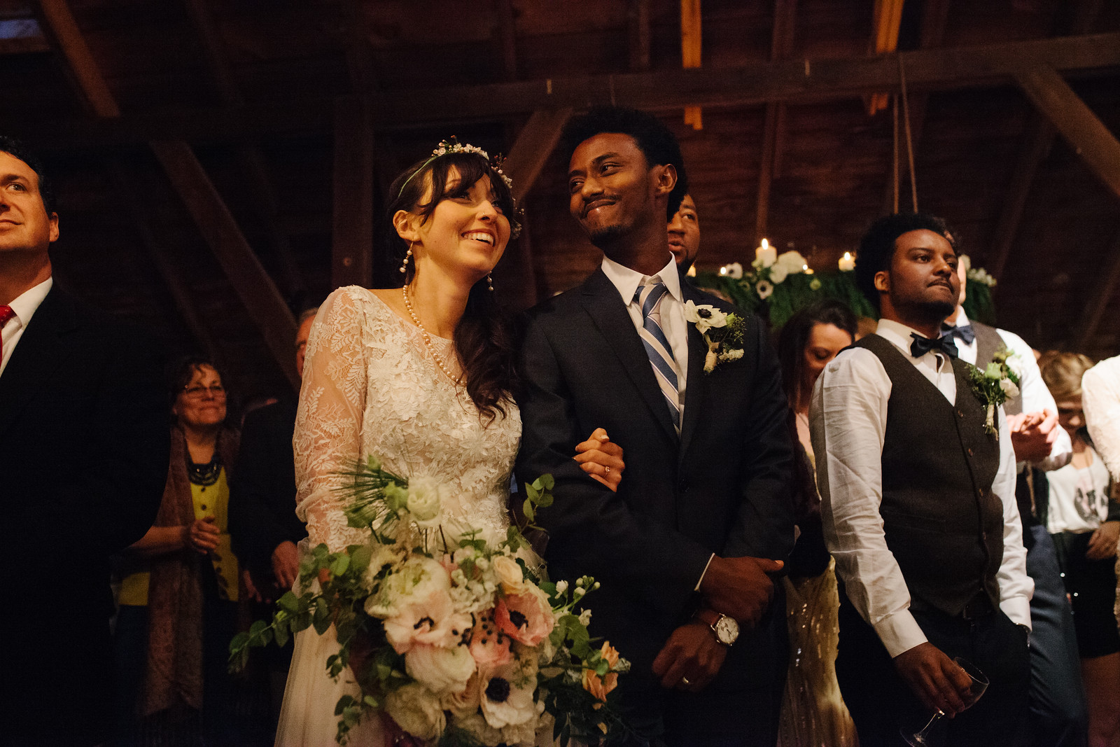 A black groom and white bride holding her bouquet and laughing happily at their barn wedding