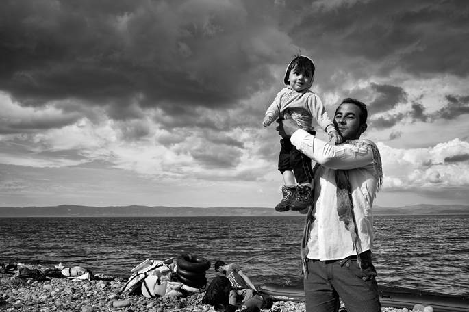 Lesbos, Greece, 2015: A father celebrates his family's safe passage to Lesbos after a stormy crossing over the Aegean Sea from Turkey. ©Tom Stoddart
