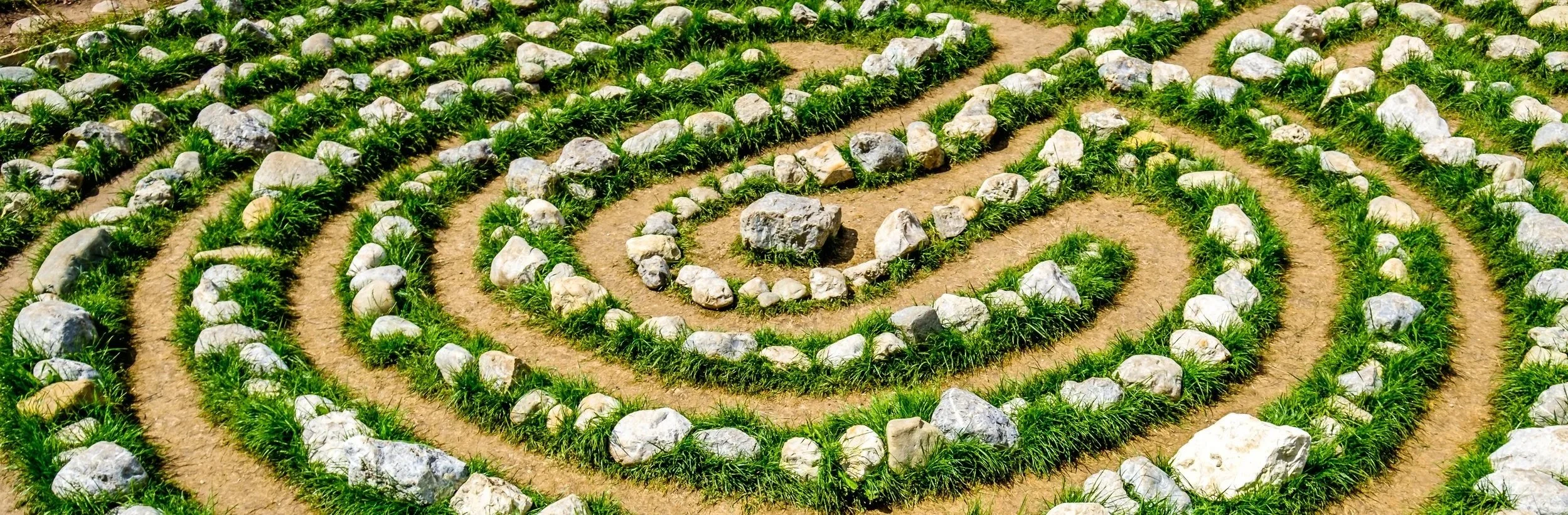 A prayer labyrinth composed of green grass, stones, and dirt.