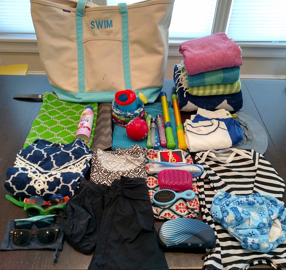 fully unpacked. It all goes in the tote. Back row: tote and towels. Second row: wet bags, sunscreen on top; mesh duffel with piles of toys on top; big kid's swimsuit, rash guard, and hat. Third row: my swim coverup, above goggles and sunglasses; my swimsuit and rash guard; diaper clutch with uno, soap case and brush on top, sitting above the prescription goggle case; little one's oldey timey bathing suit and swim dipe.