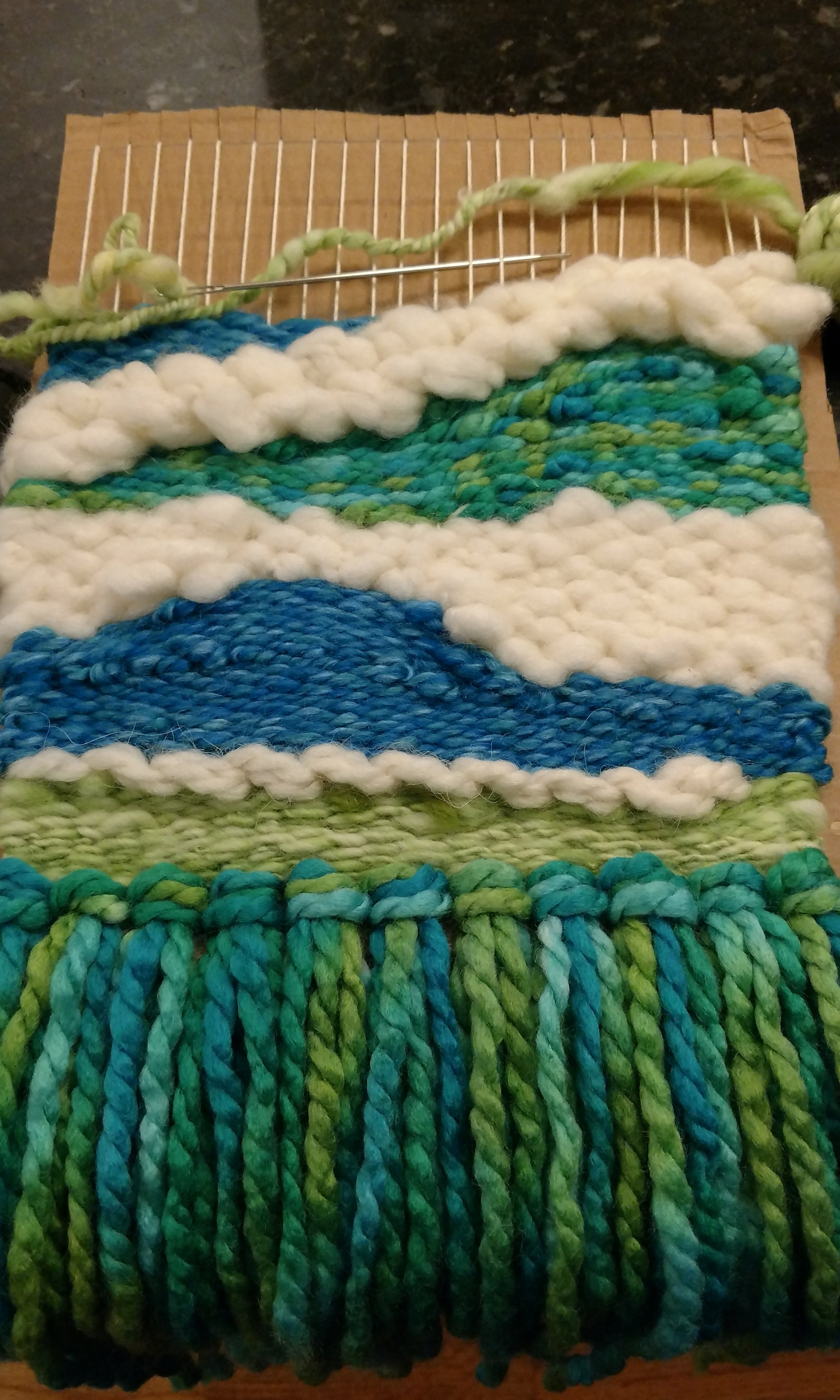 work in progress, featuring rya knots, soumak, and roving. The big puffy white section is wool roving, the narrow line of white is a line of soumak weaving in a chunky yarn. The rya knots make a fringe.