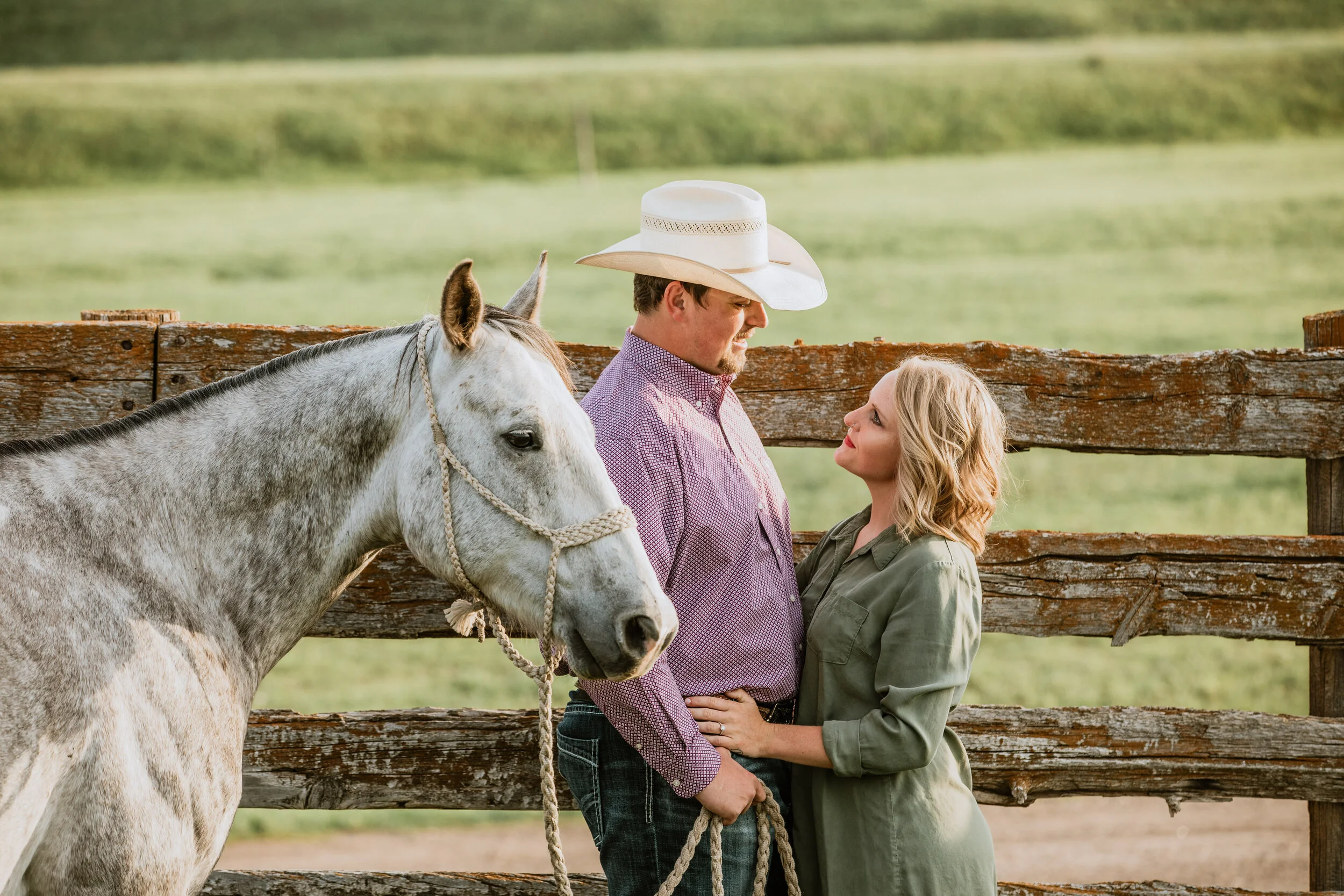 girl wearing olive green with fiancé wearing purple and a cowboy hat standing with their white horse