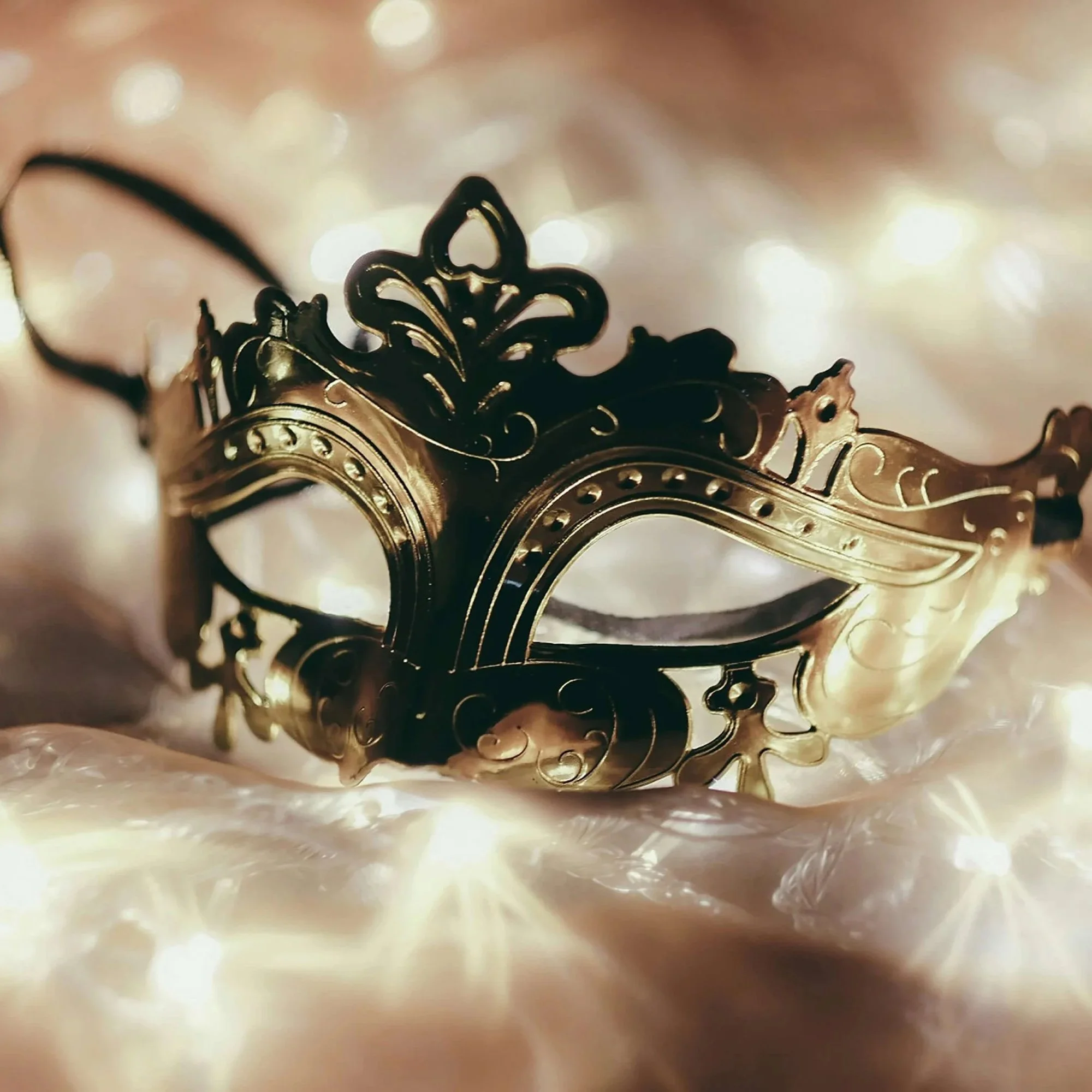 Decorative golden eye mask laying on white tulle.