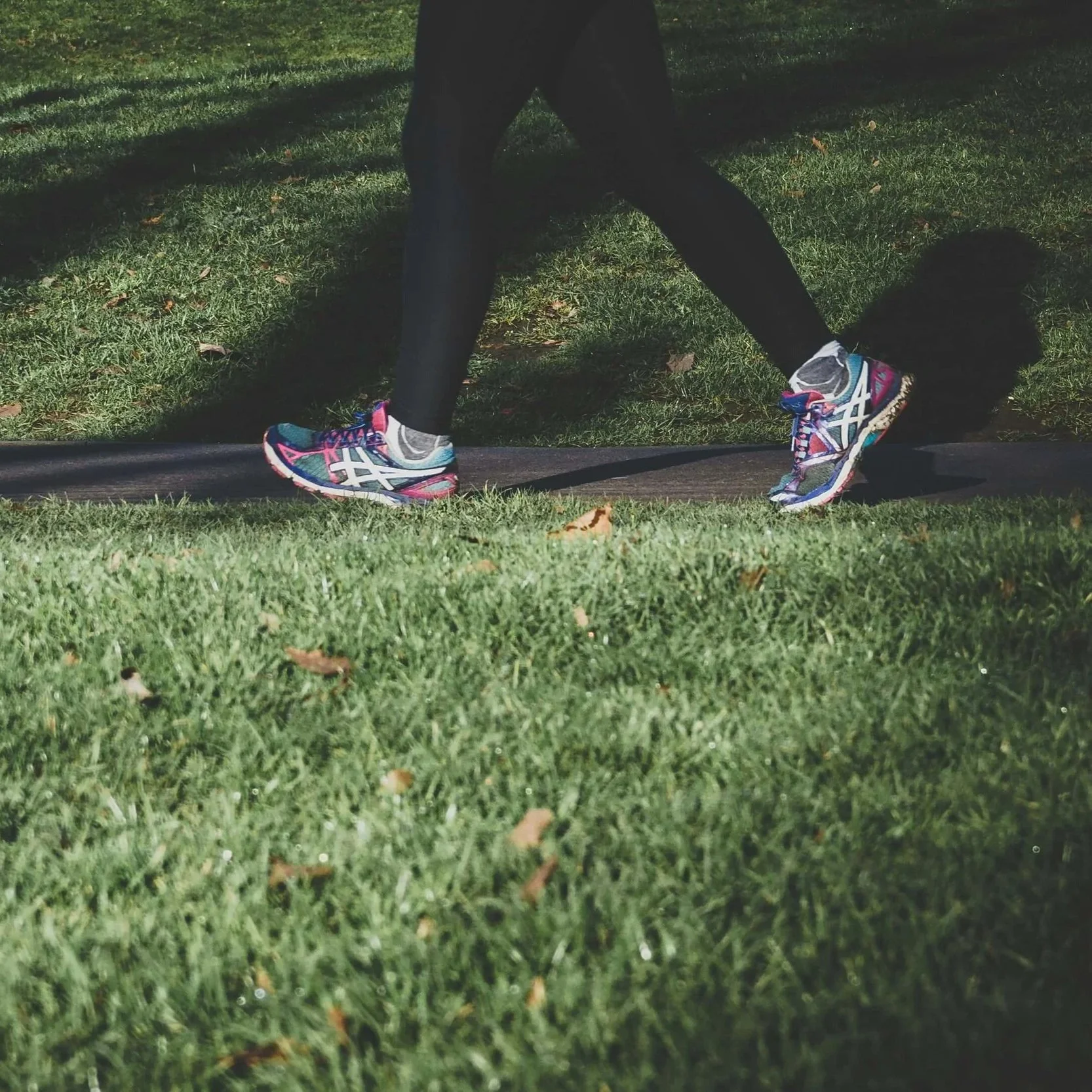 Person's lower legs wearing sneakers walking on sidewalk.