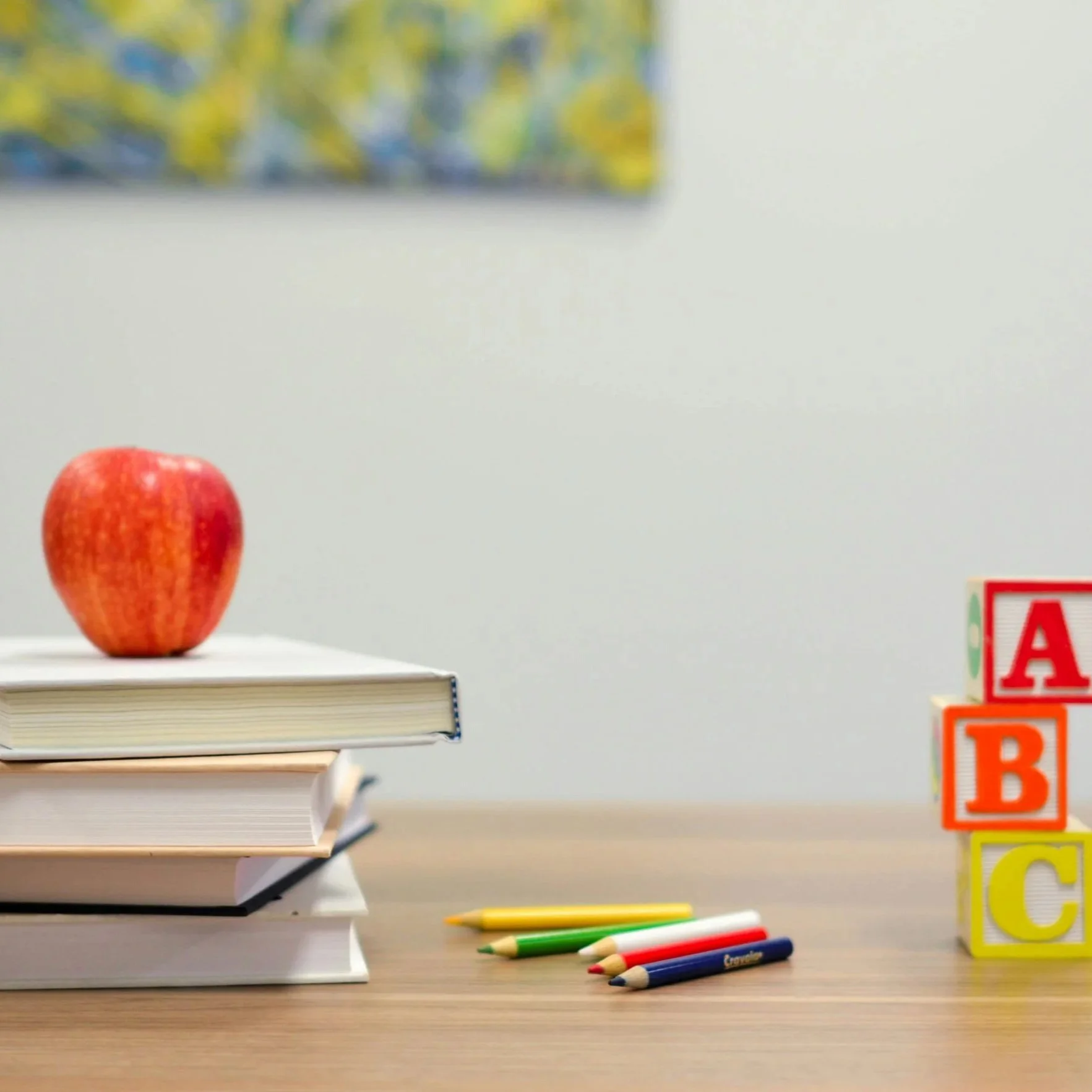 Books stacked on desk with apple on top alongside pencils and ABC blocks.