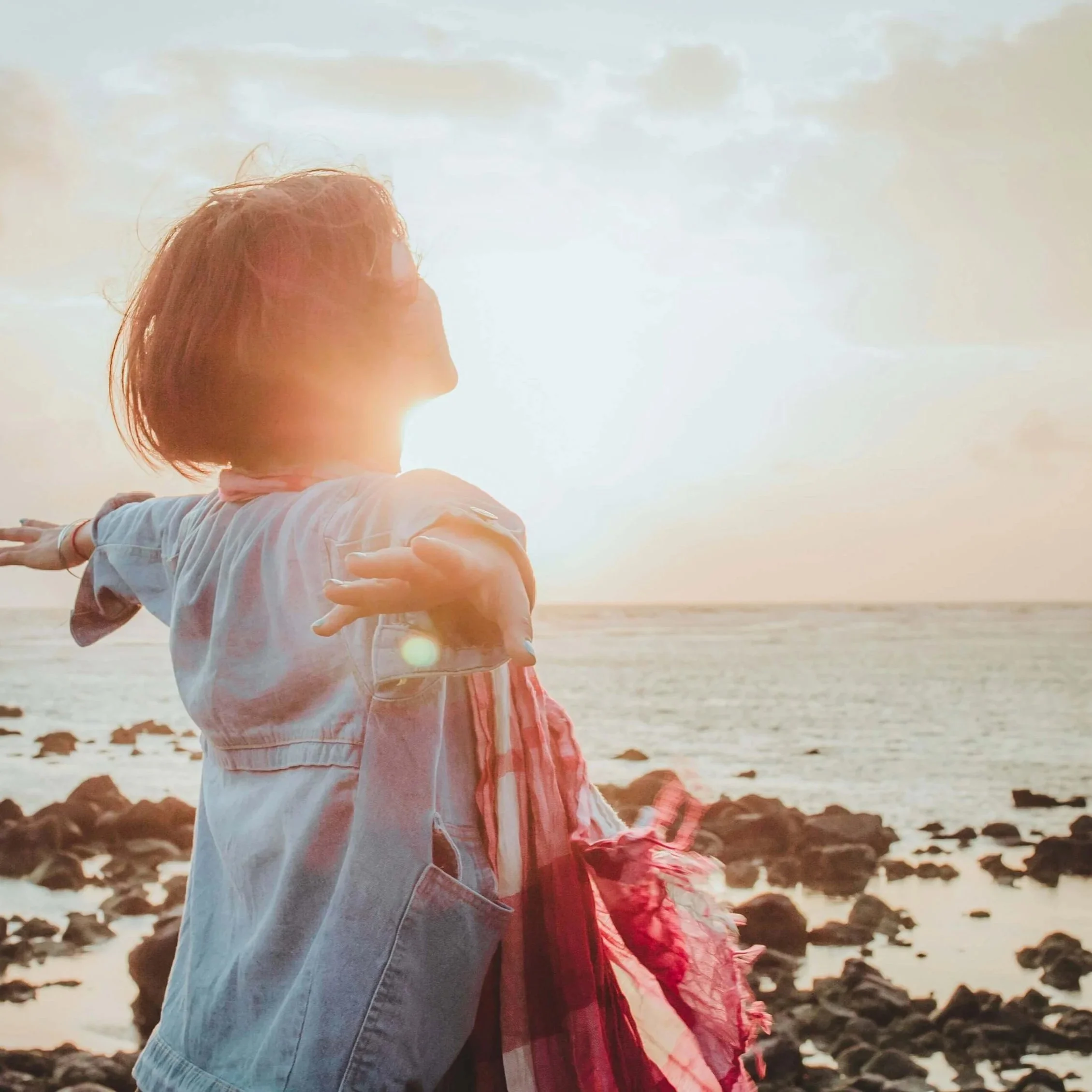 Woman with outstretched arms facing the sun.