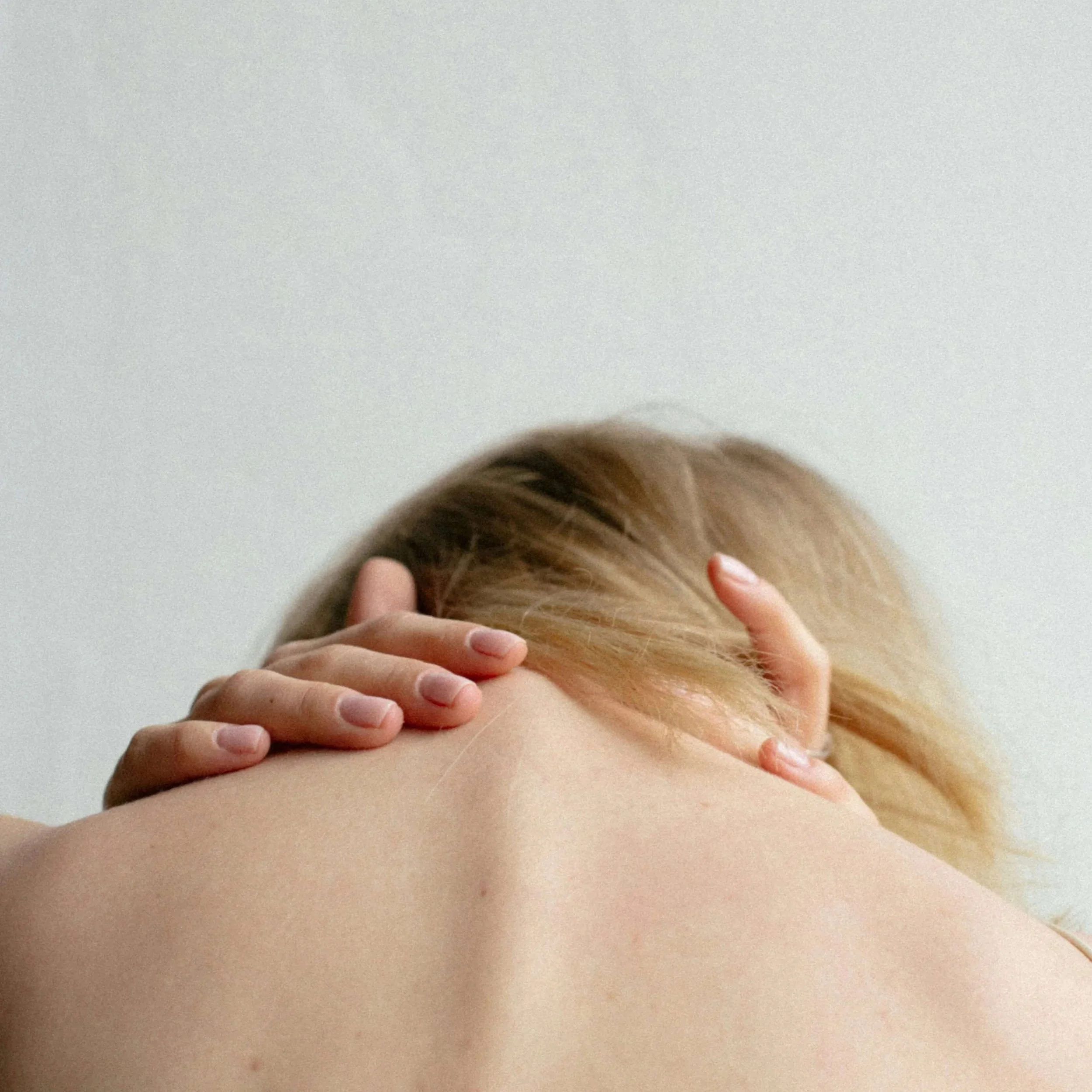 Back of blonde haired woman bent over holding her neck.