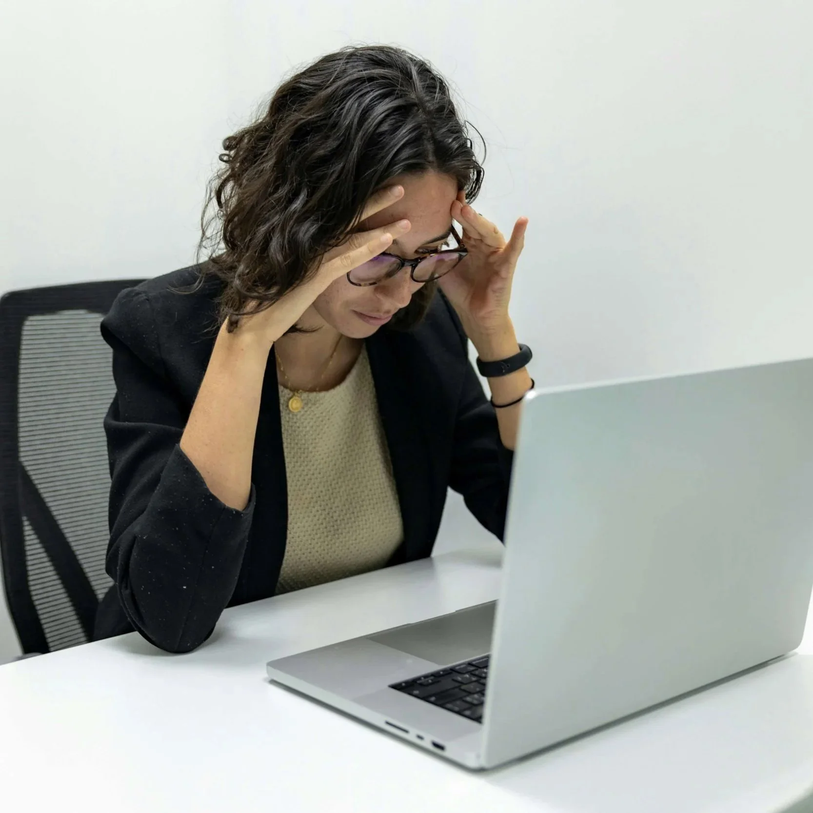 Woman with her forehead in her hands looking down at laptop.