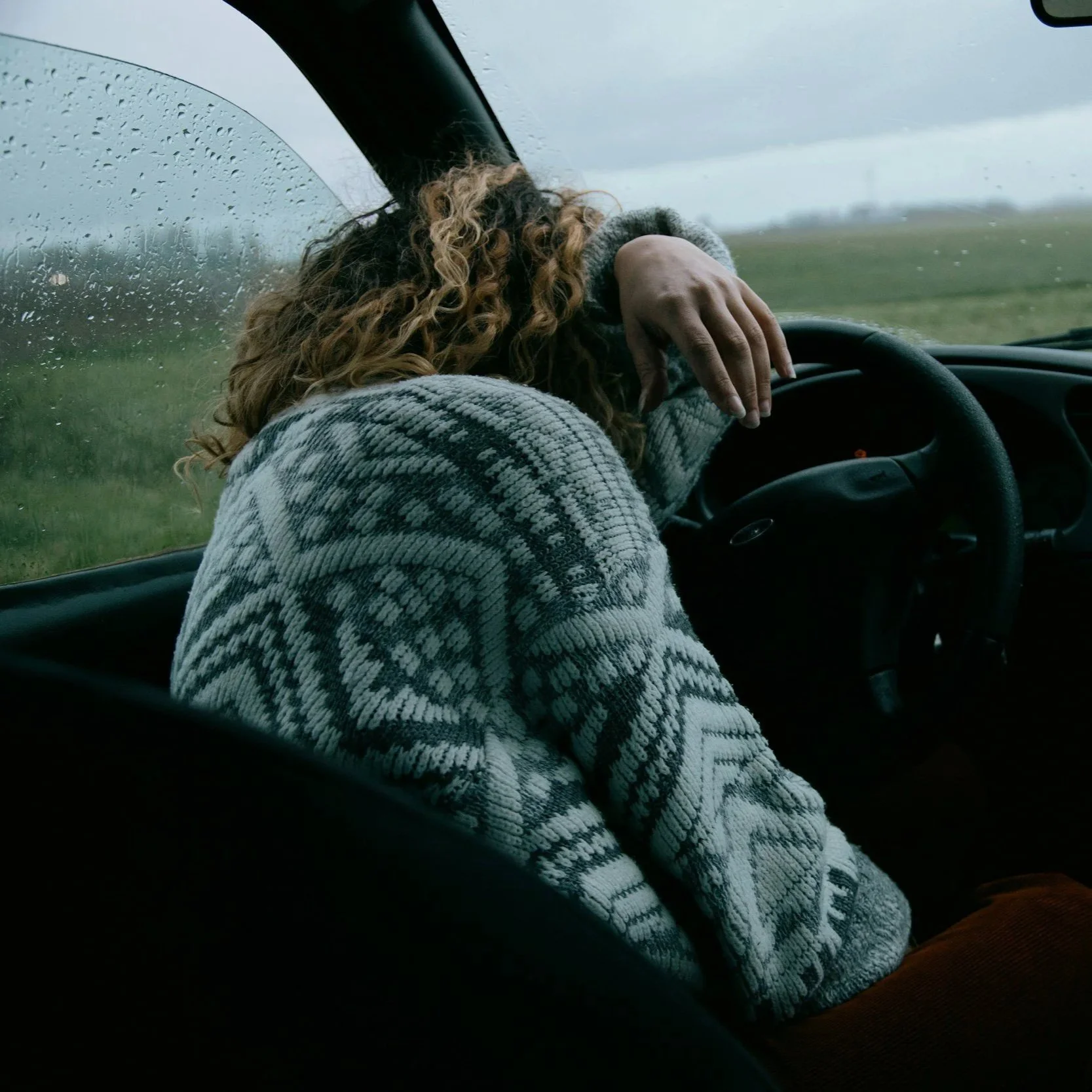 Woman sitting in car with her head down on steering wheel.