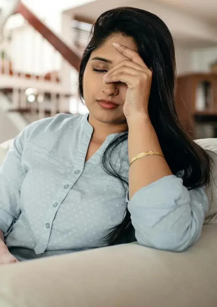 Woman with hand half over face with closed eyes.