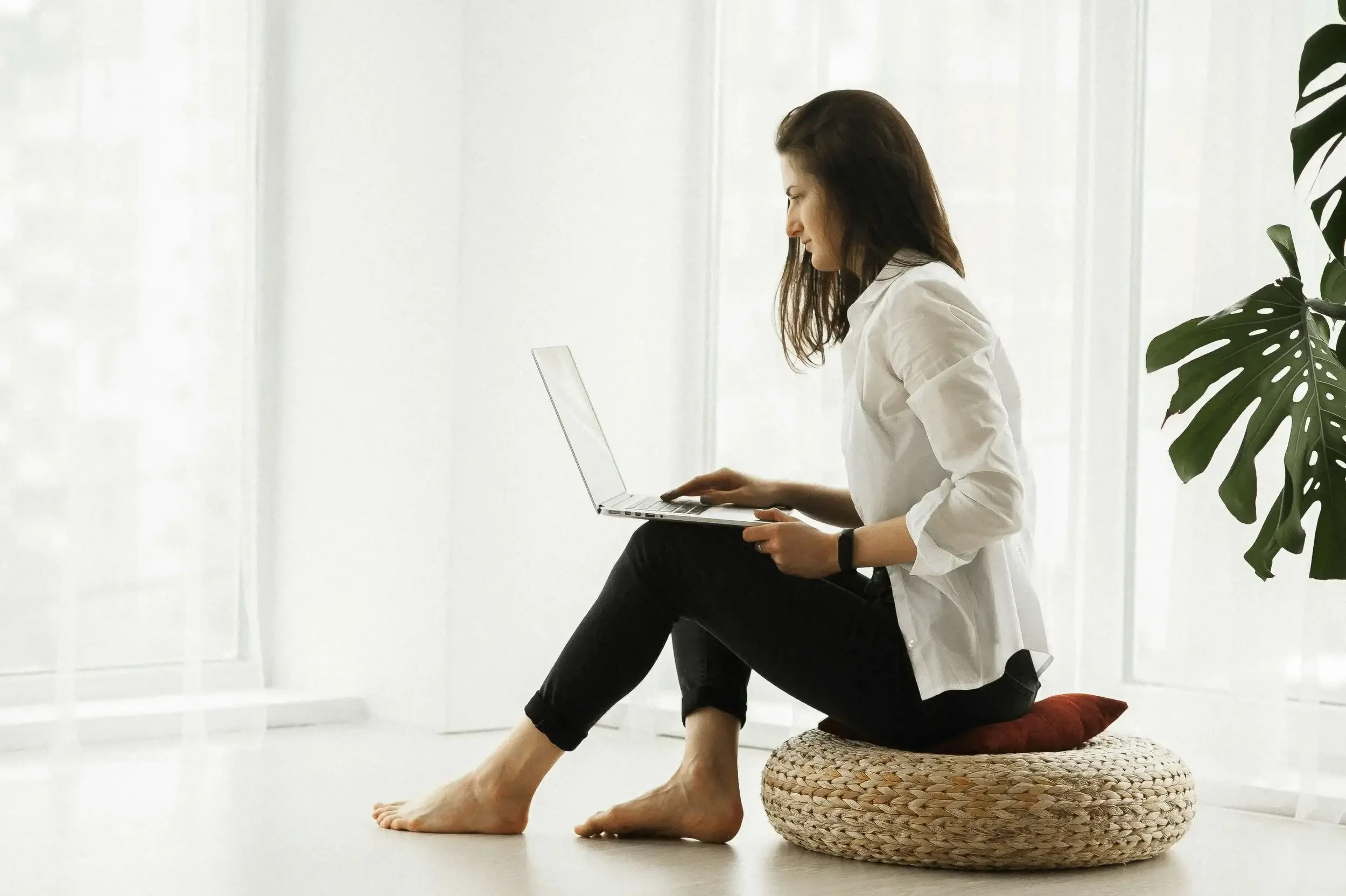 Woman sitting on floor cushion on computer.