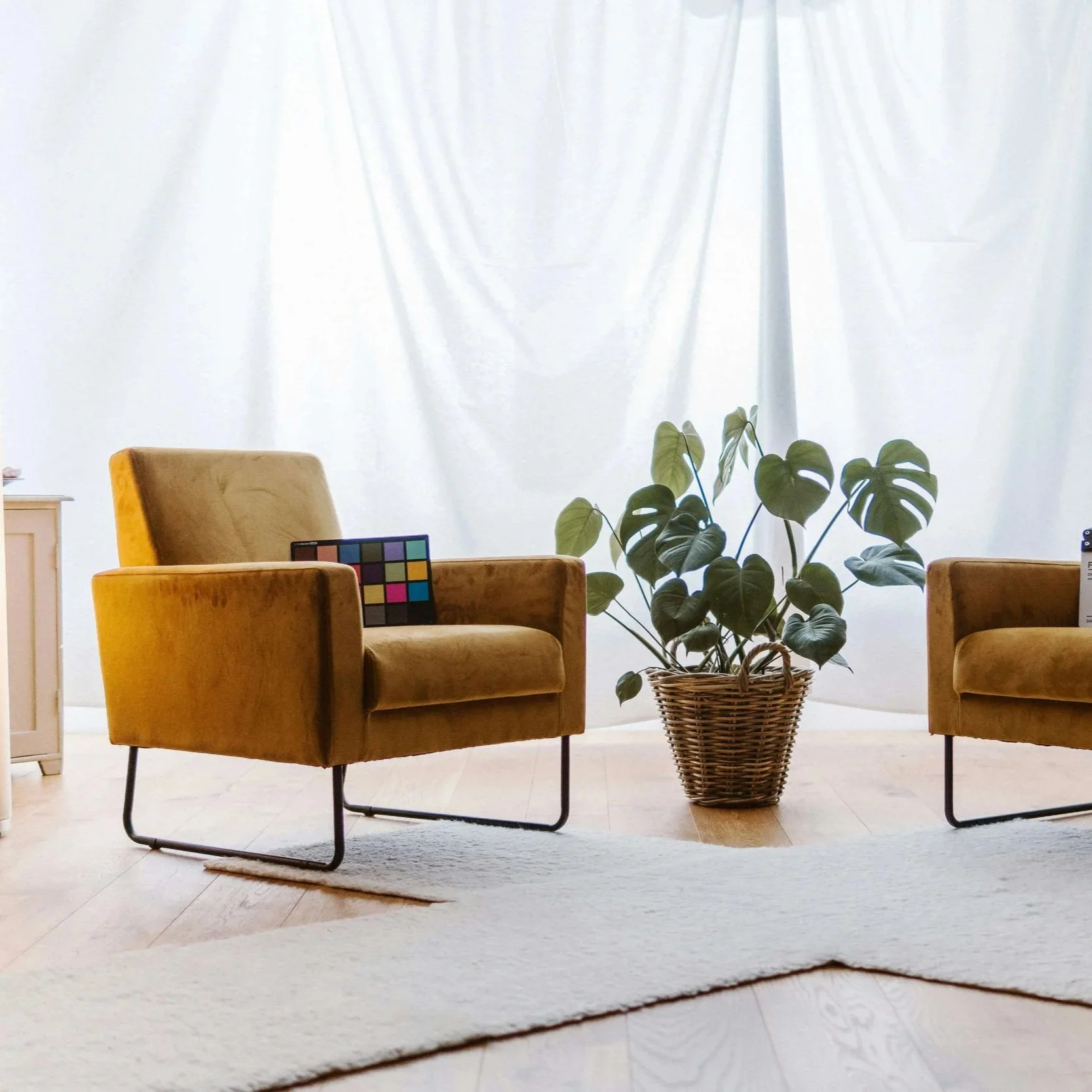 Tan chair in a bright white room with soft drapes and another chair off to the side.