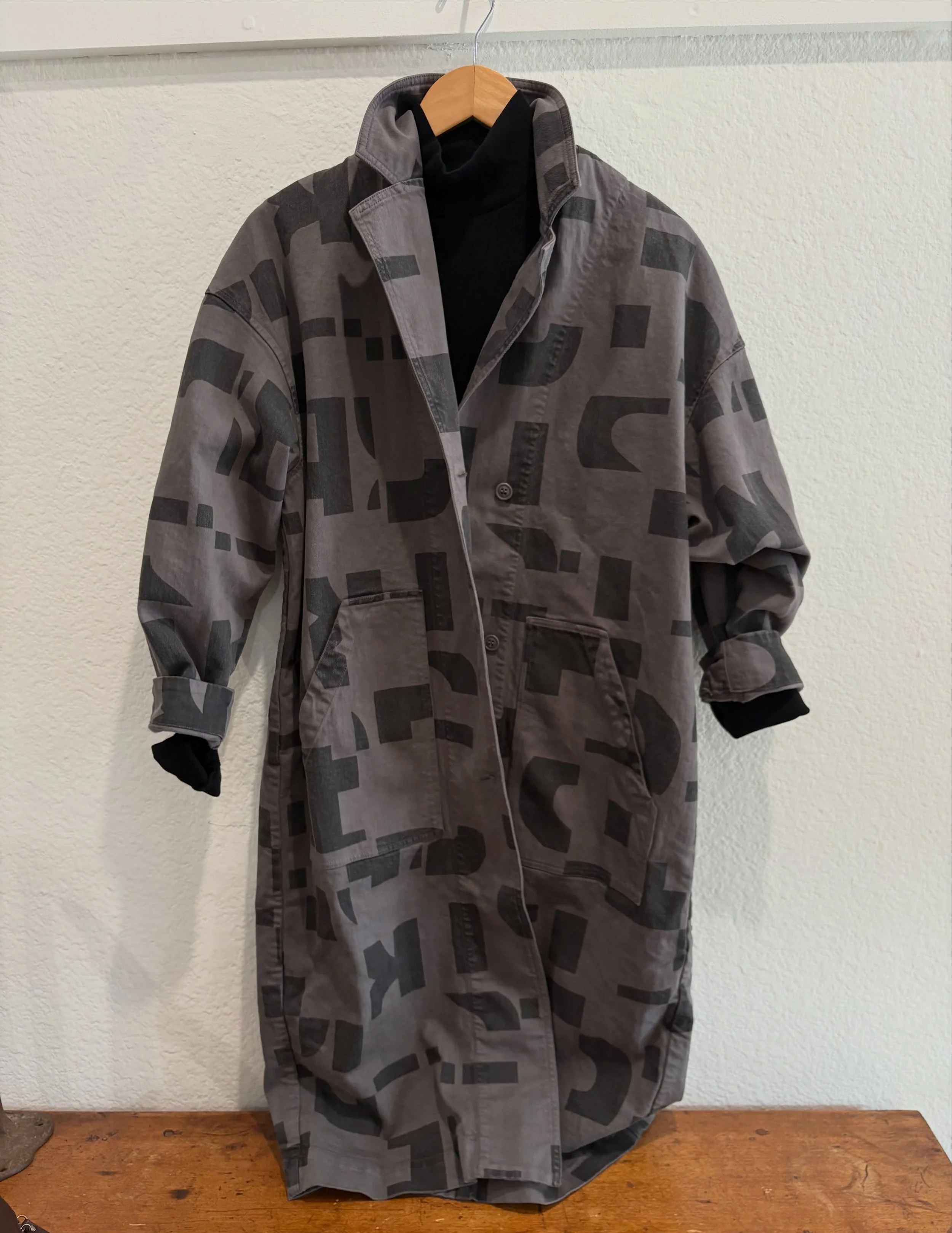 The Catalyst Trench in recycled cotton/spandex twill features a sharp lapel, oversized patch pockets, exaggerated length, and structured topstitching for bold dimension. Designed to layer over everything&mdash;from denim to silk shirting&mdash;it bri