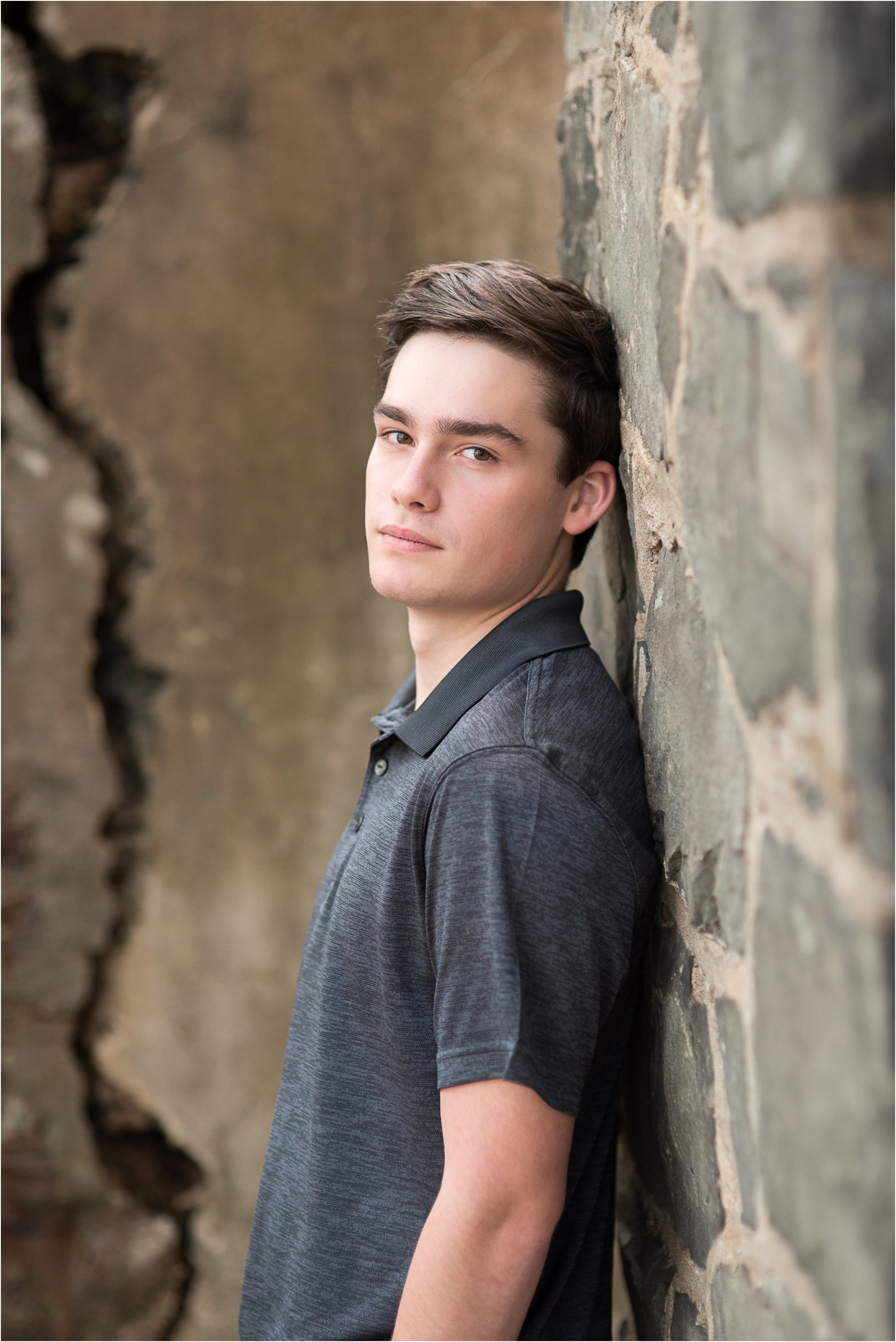 Lynchburg senior stands up against a stone wall looking at the camera with a serious look on his face and hands in his pockets. Karin Nicole Photography - Lynchburg Photographer
