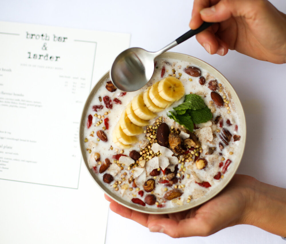 Bowl of gluten-free muesli topped with banana, goji berries, and mint, beside a menu