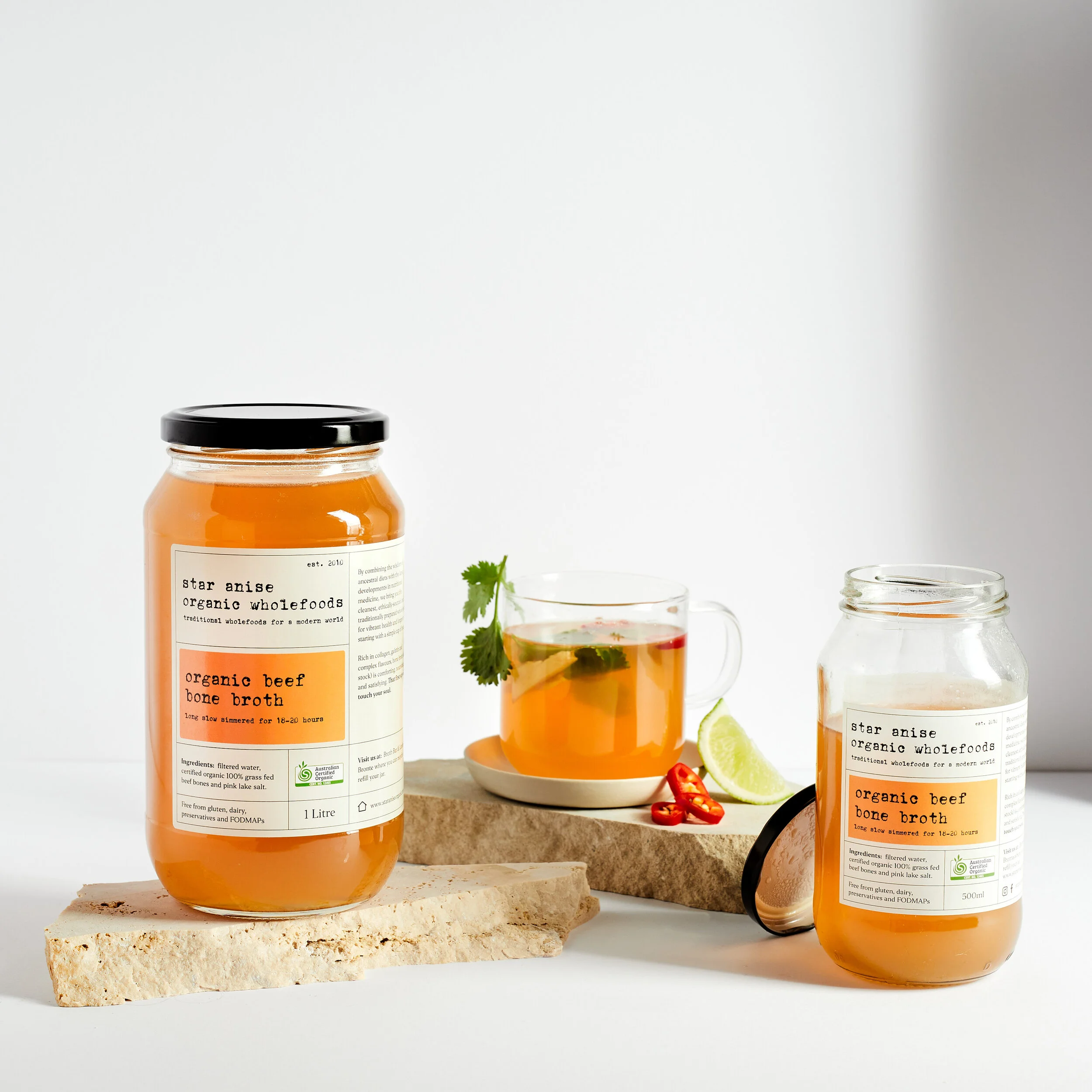 Glass jars of certified organic beef bone broth with mug, lime, and herbs – halal, grass-fed, and made in Sydney